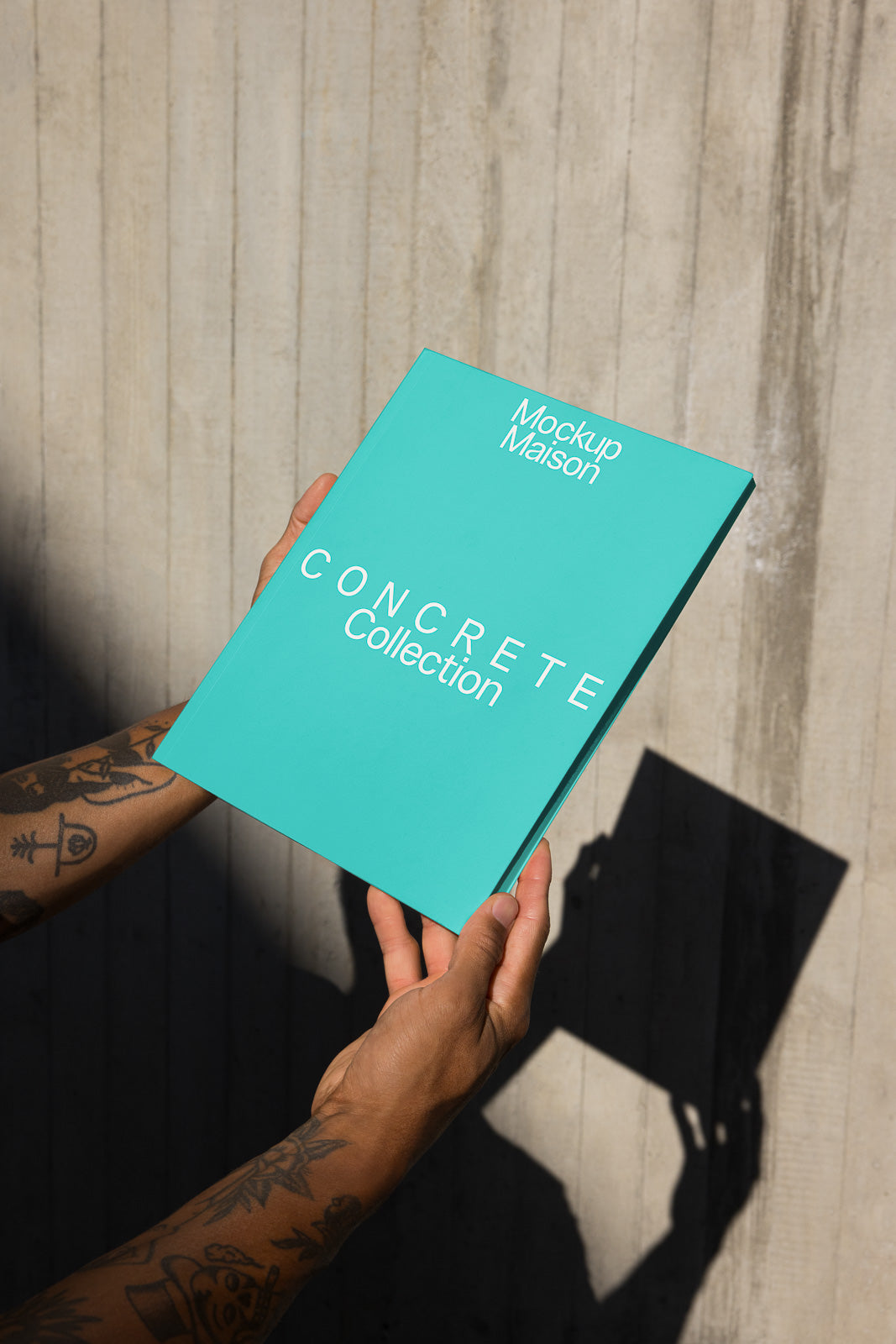 PSD mockup of a turquoise book titled "Concrete Collection" held by tattooed hands against a textured concrete background.