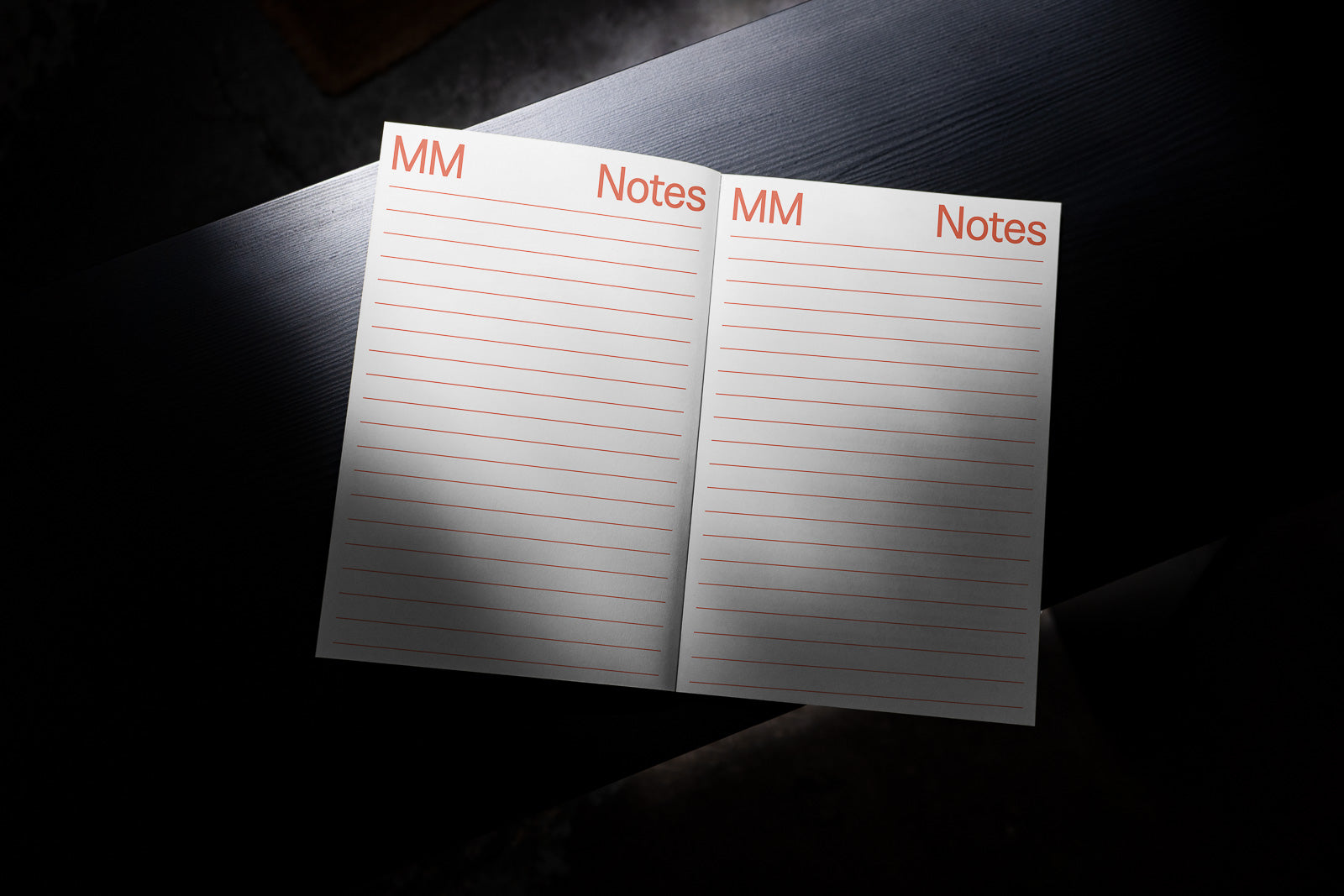 PSD mockup of an open notebook showing lined pages labeled "MM" and "Notes" in orange text, placed on a dark surface with soft shadows.