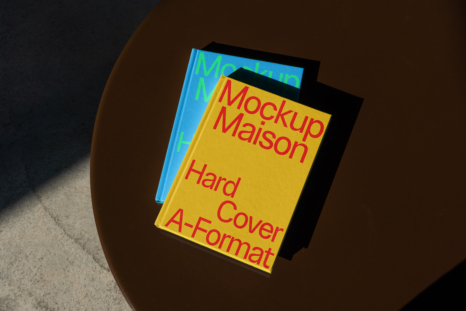 PSD mockup of two hardcover books on a round brown table, with one book in bright yellow and bold red text and the other in blue with green text.