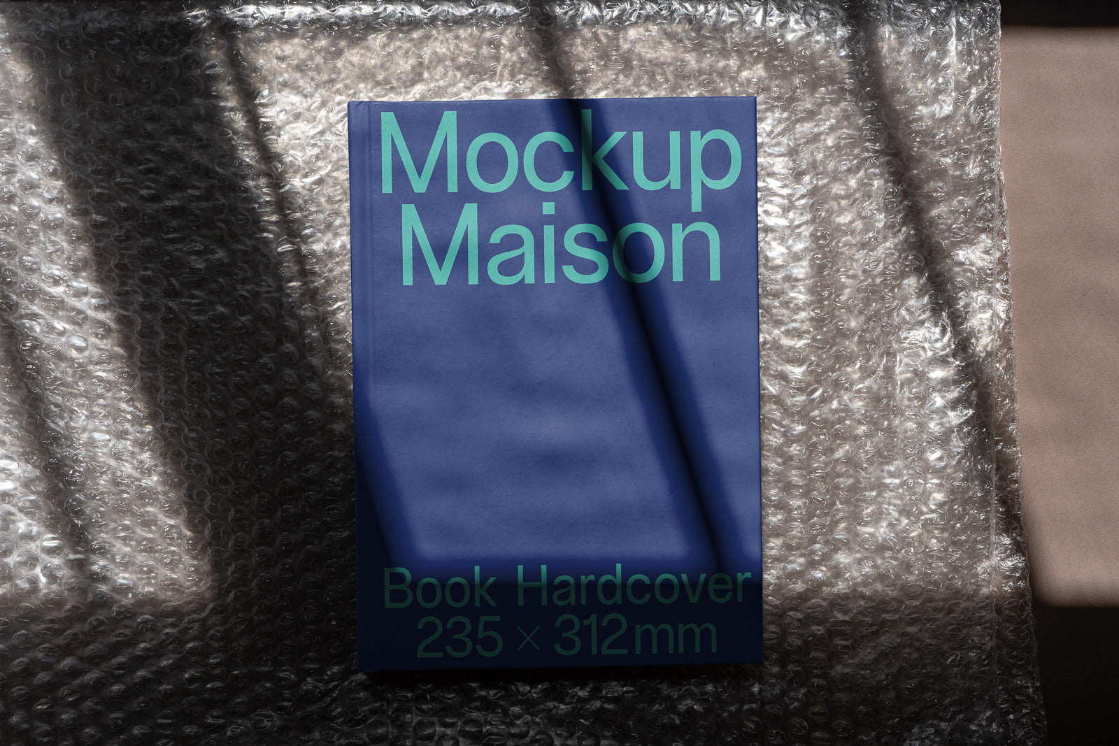 PSD mockup of a hardcover book titled "Mockup Maison" with dimensions 235 x 312 mm, displayed on bubble wrap with a shadow pattern.
