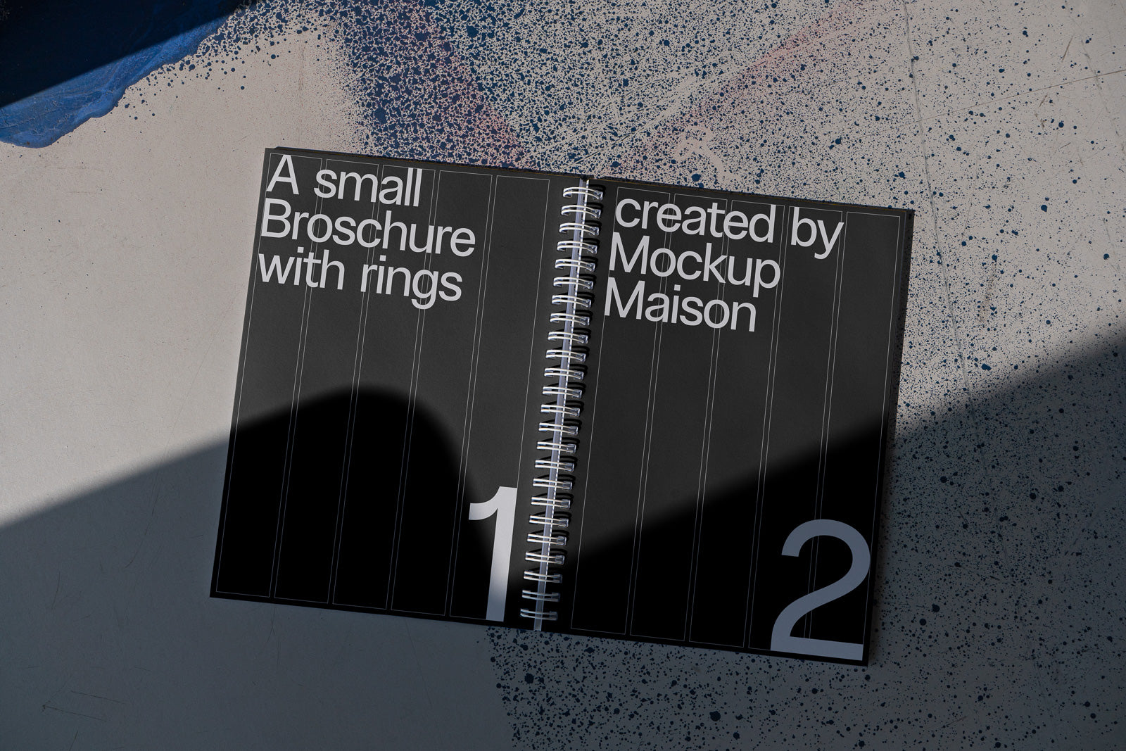 PSD mockup of an open spiral-bound brochure on a textured surface, displaying the text "A small Broschure with rings created by Mockup Maison" with shadows.