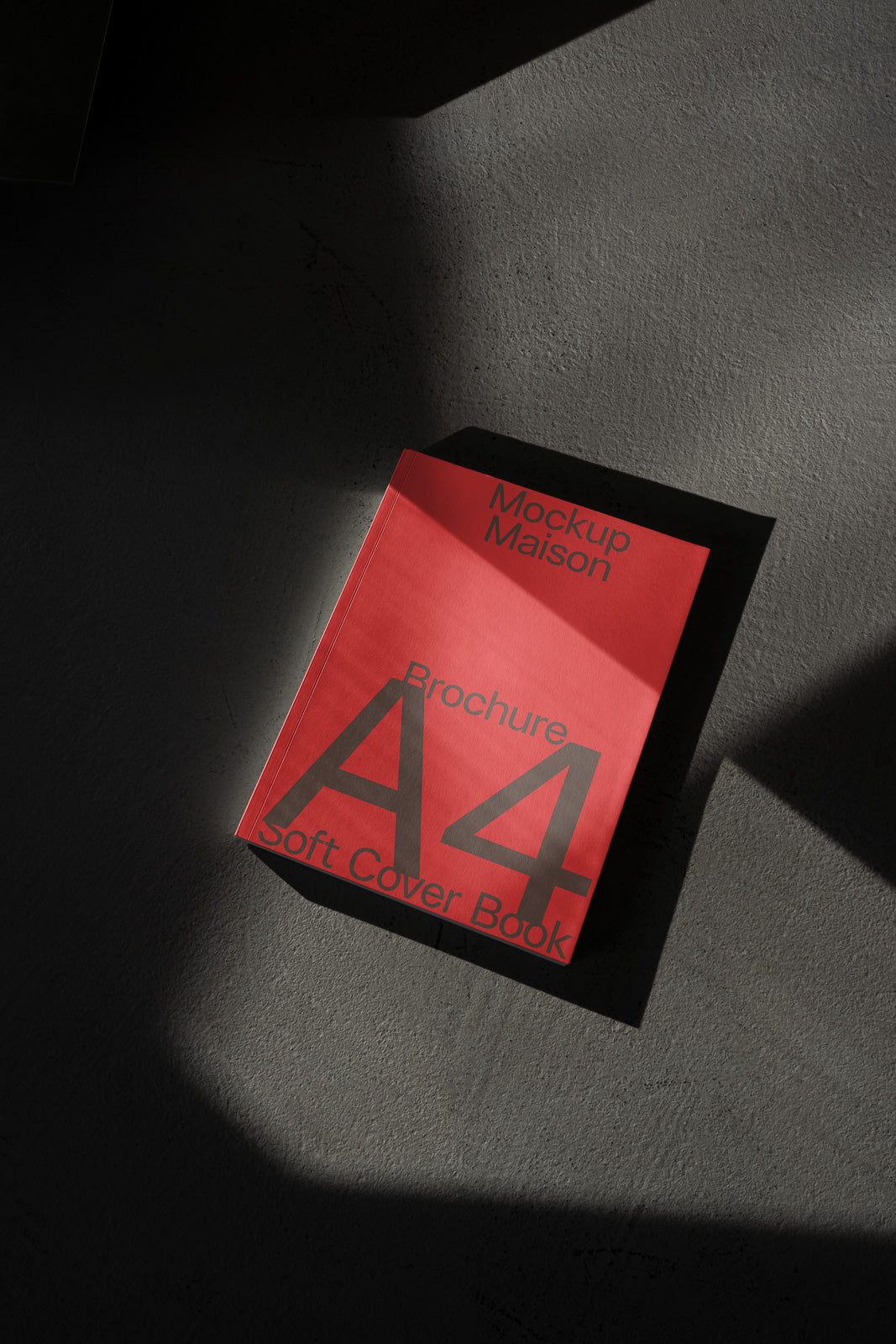 PSD mockup of an A4 soft cover book with a red cover titled "Brochure" and "Mockup Maison," casting shadows on a textured surface.