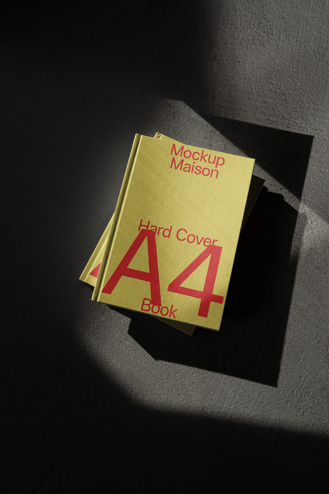 PSD mockup of a yellow A4 hardcover book with red text, titled "Mockup Maison," placed on a textured gray surface with dramatic lighting and shadow.