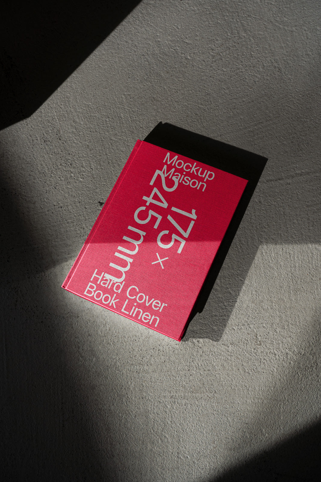 PSD mockup of a red hardcover book linen, 175x245 mm, with prominent shadows cast on a textured surface.