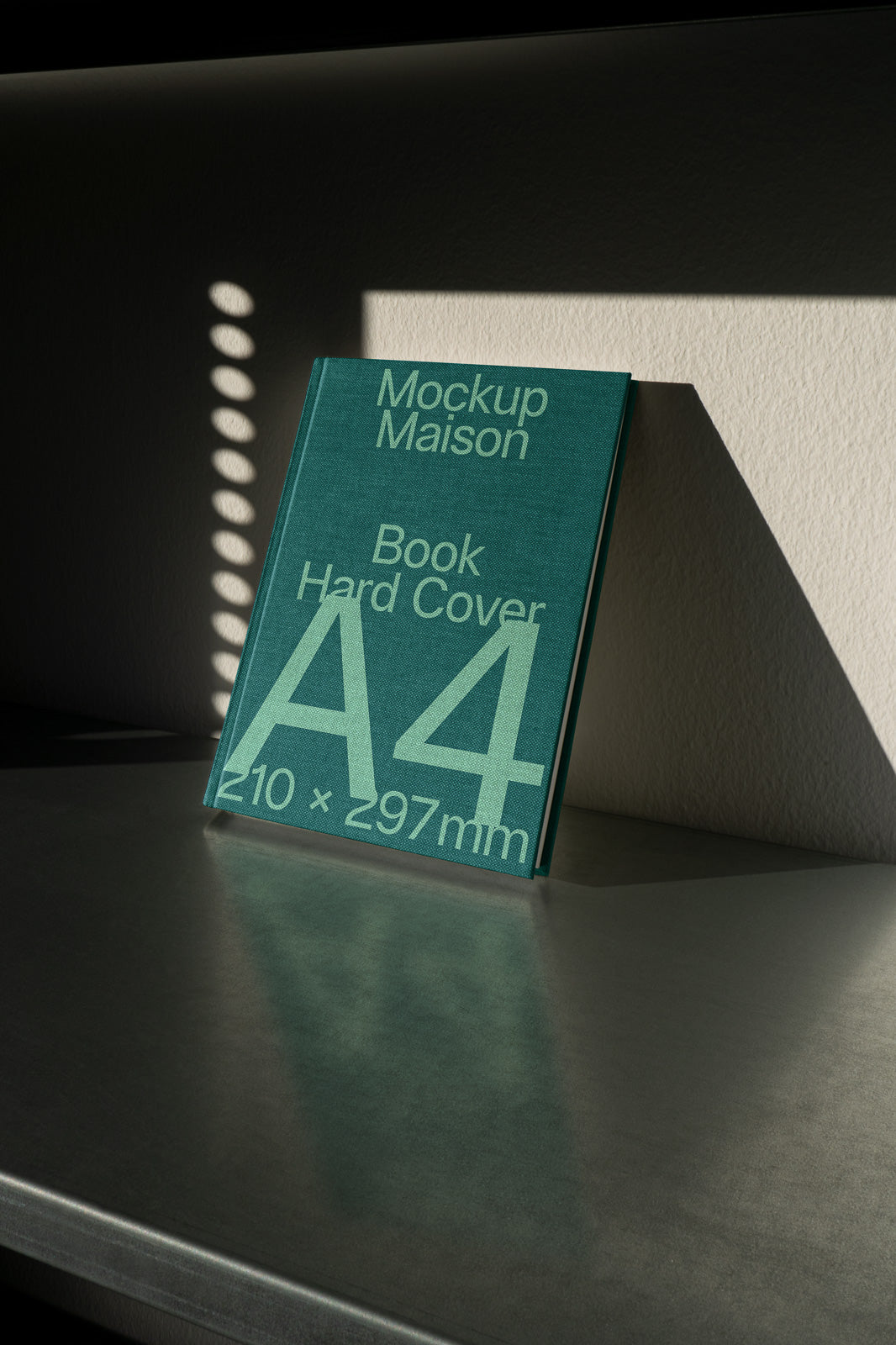 PSD mockup of a green A4 hard cover book titled "Mockup Maison" with dimensions 210 x 297mm, leaning against a wall on a shadowed surface.