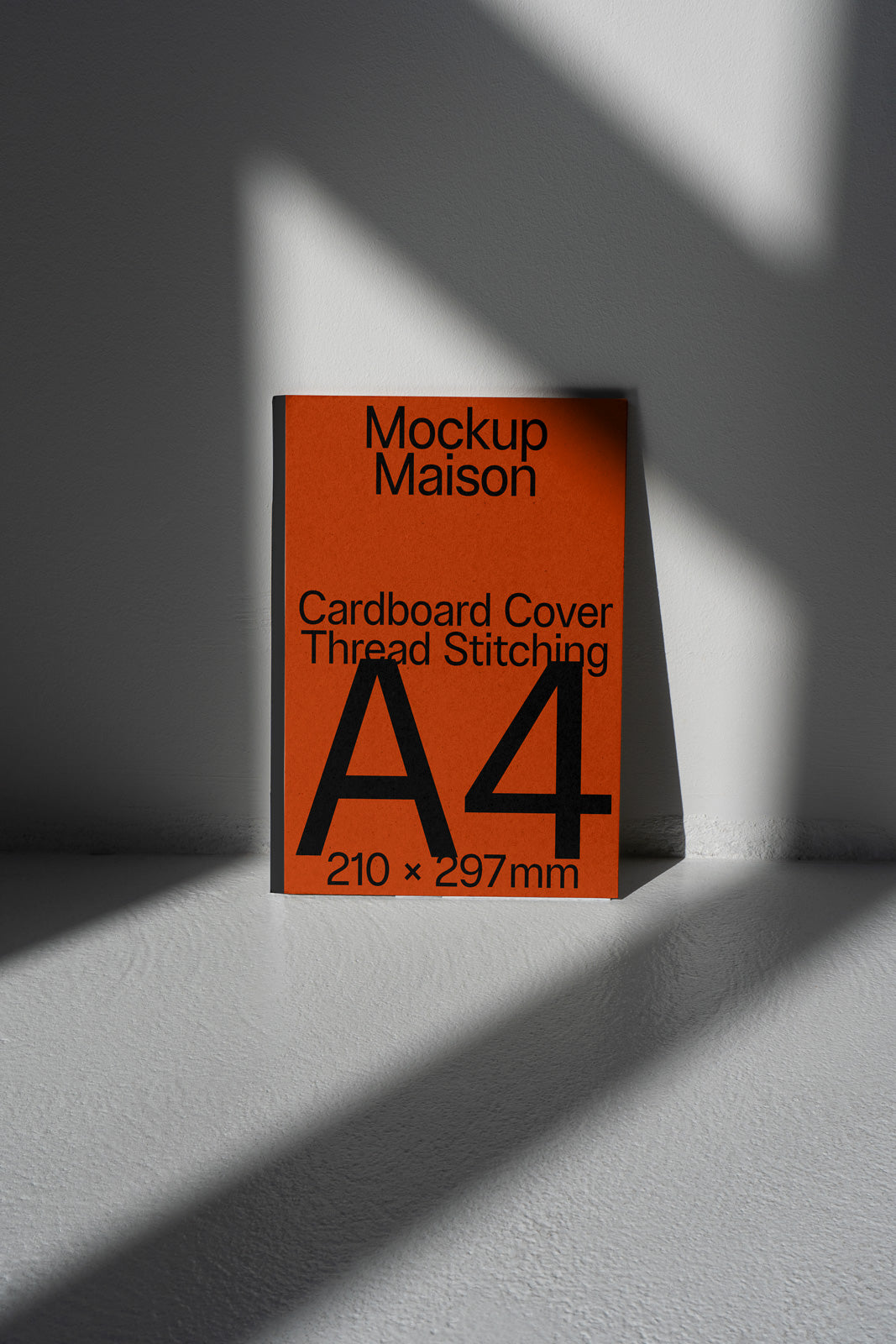 PSD mockup of an A4 cardboard cover with thread stitching against a gray wall, featuring bold text and geometric shadows.