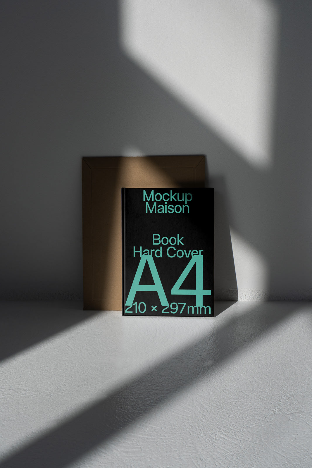 PSD mockup of a hardcover A4 book labeled "Mockup Maison" against a cardboard backdrop with soft shadows on a light surface.
