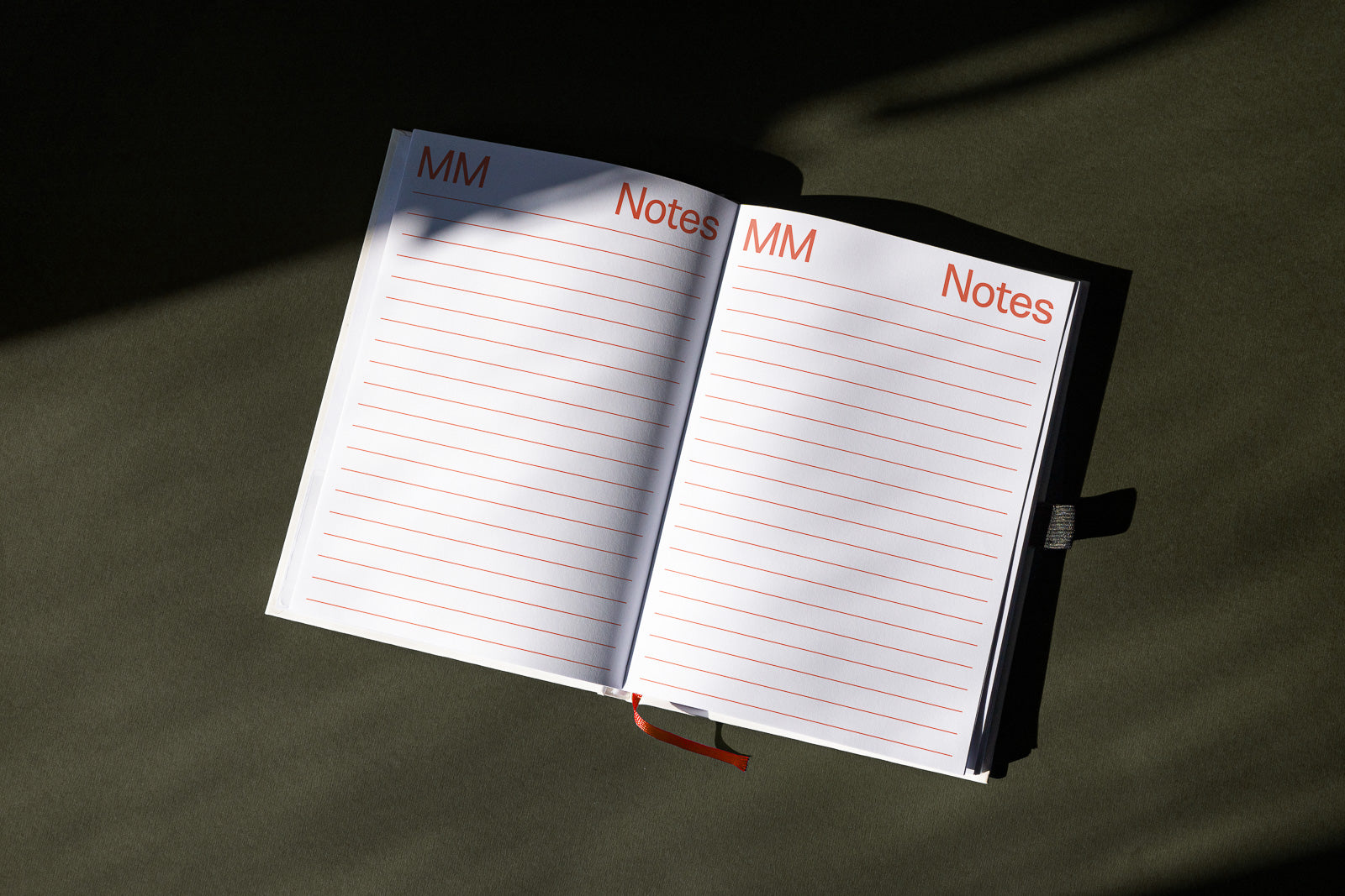 PSD mockup of an open notebook with red-lined pages, labeled "MM" and "Notes" at the top, lying on a dark surface with shadows.