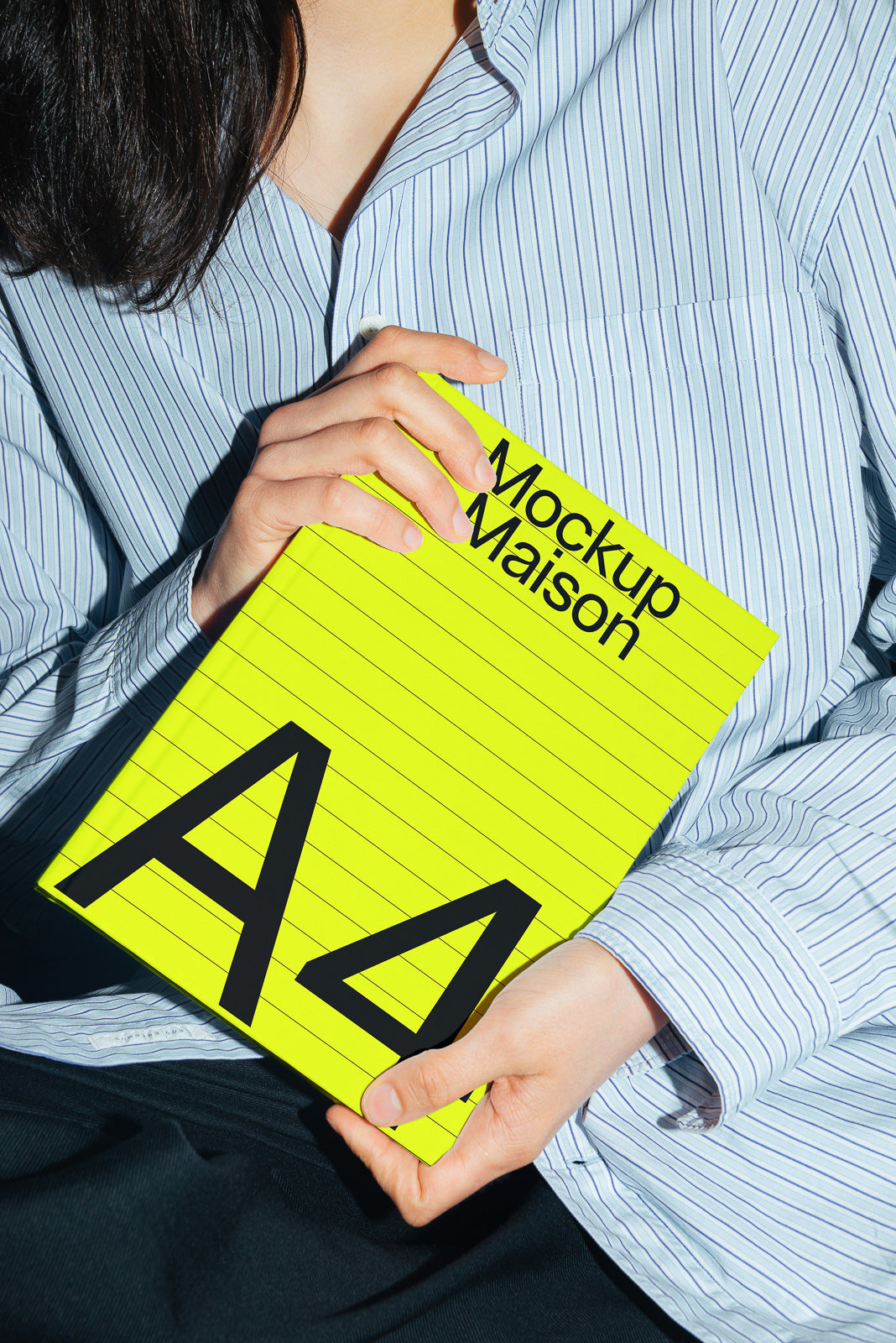 PSD mockup of a person wearing a striped shirt holding a bright yellow A4-sized notebook labeled "Mockup Maison," with diagonal lines.