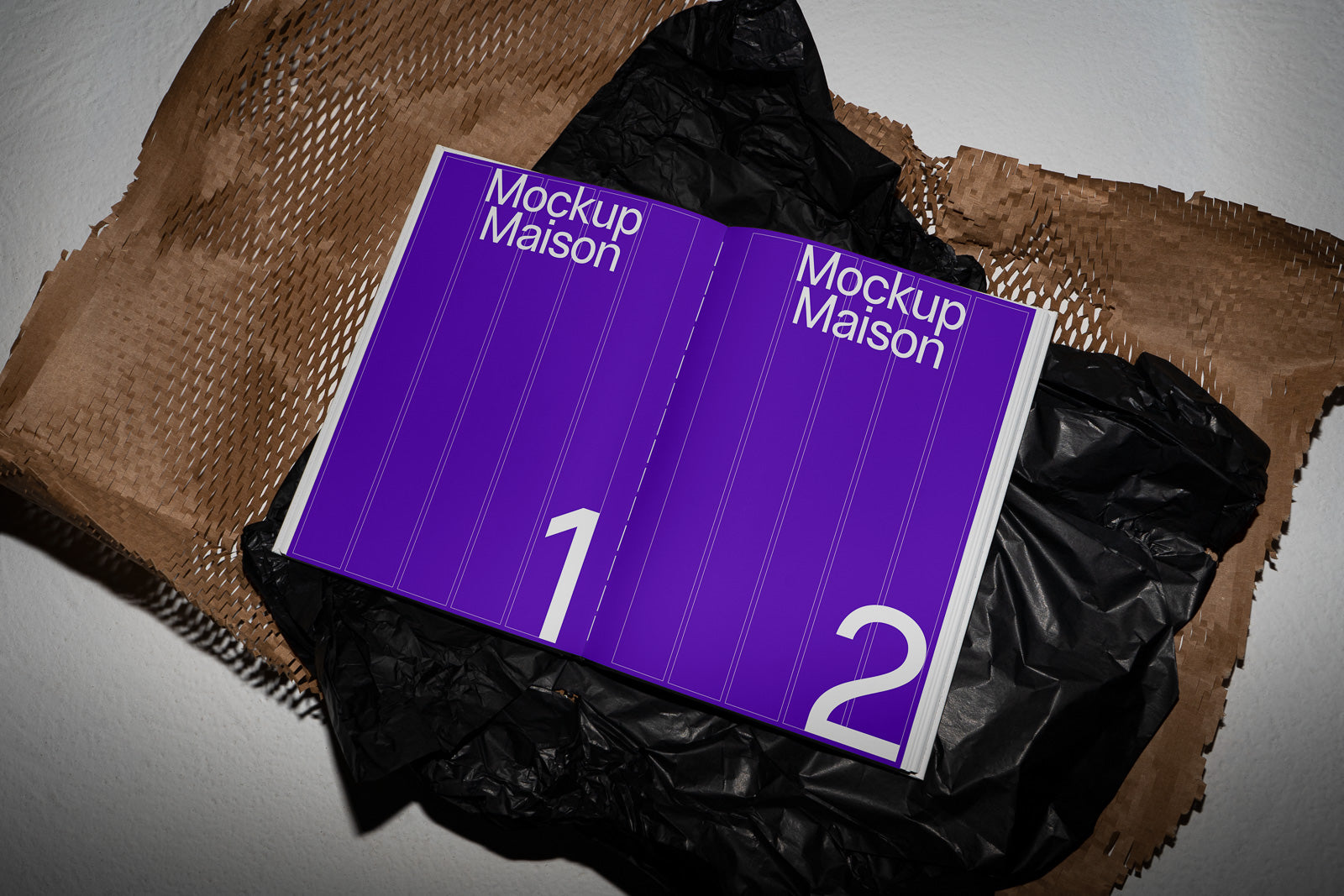 PSD mockup of an open booklet featuring purple pages with the text "Mockup Maison" and large numbers "1" and "2", placed on crumpled black and brown packaging material.