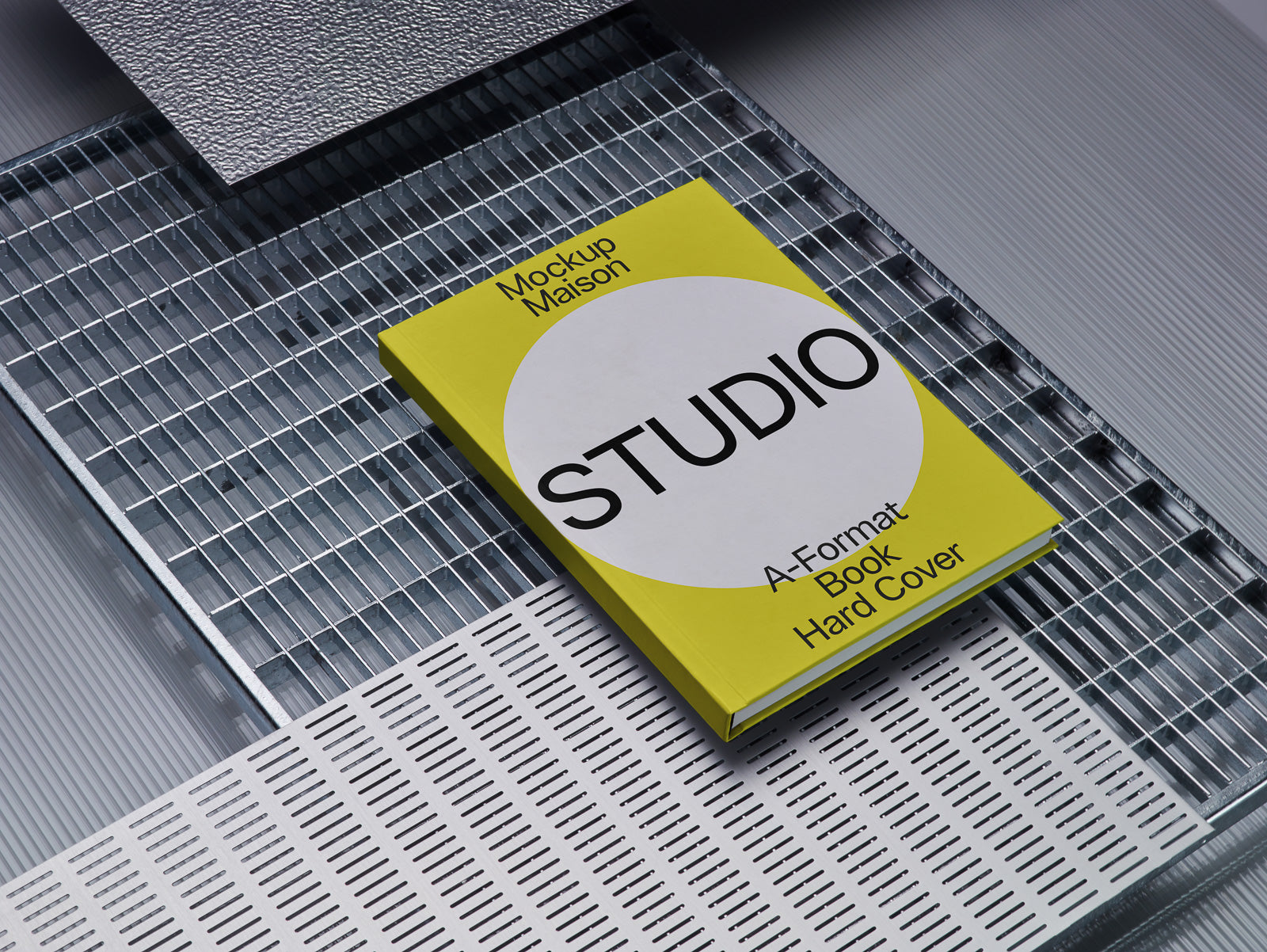 PSD mockup of a hardcover book titled "STUDIO" with a yellow cover, placed on a metallic and textured industrial surface, showcasing modern design.
