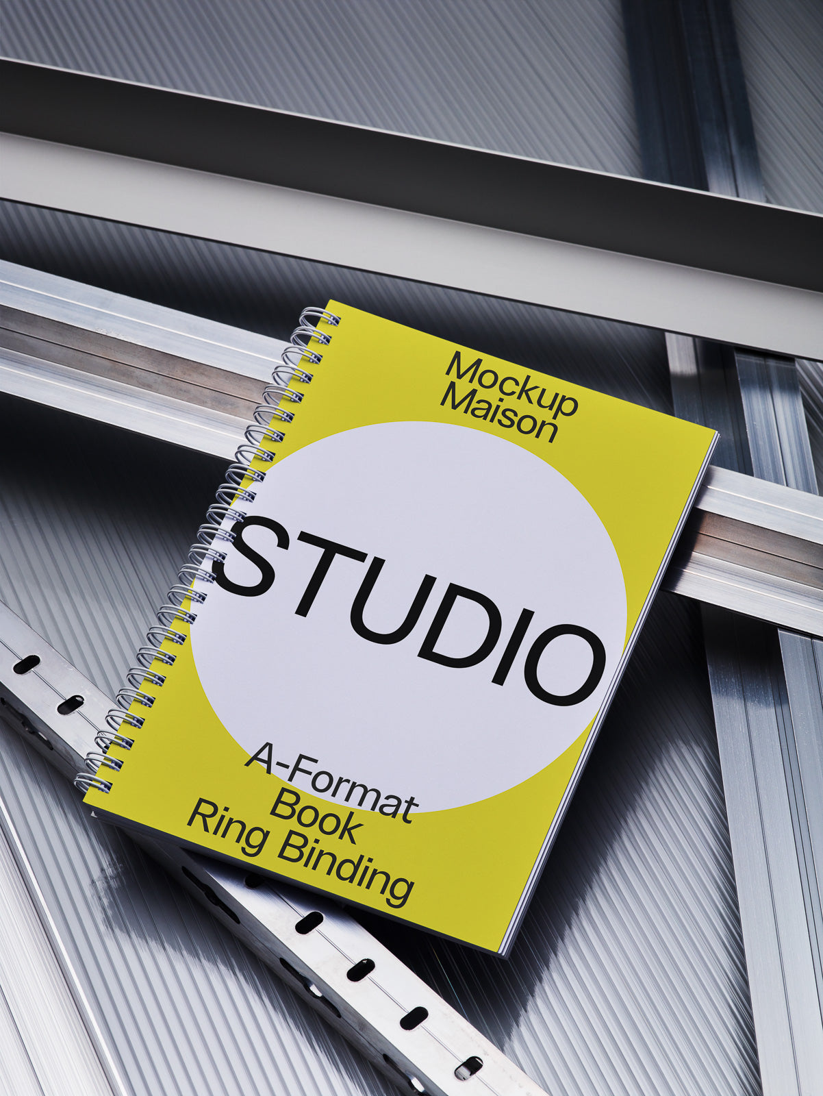 PSD mockup of a spiral-bound notebook with a yellow and white cover featuring bold text, placed on a reflective metallic surface.