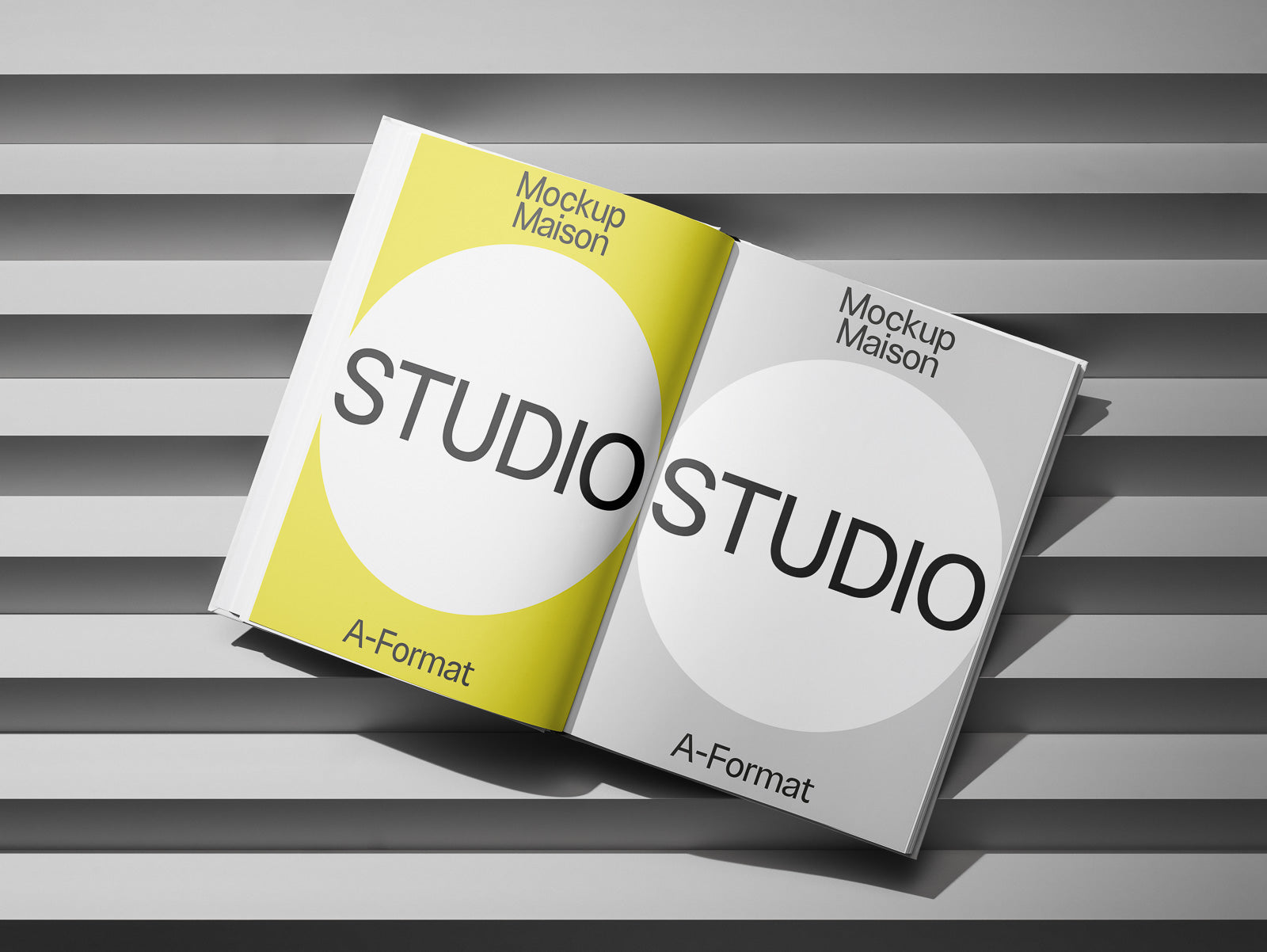 PSD mockup of an open book with pages displaying "STUDIO" text on yellow and gray backgrounds, titled "Mockup Maison A-Format," on a striped surface.