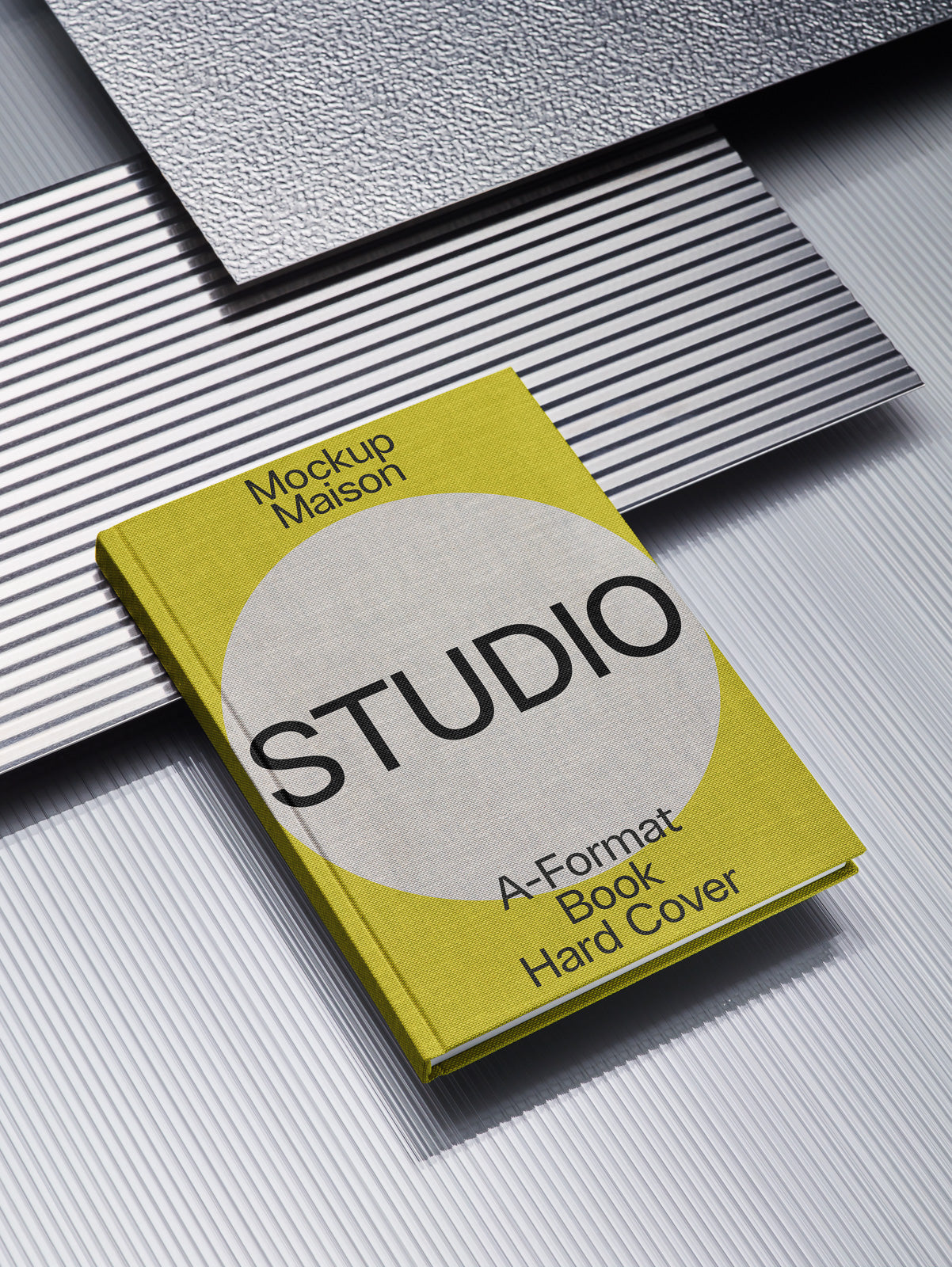 PSD mockup of a hardcover A-format book titled "Studio" by Mockup Maison, placed on textured and striped metallic surfaces.