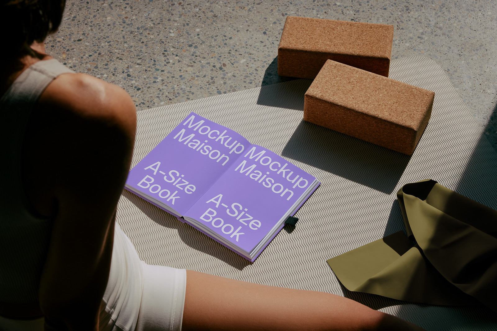 PSD mockup of an open A-size book with the text "Mockup Maison" on a patterned mat, next to cork blocks and a green fabric.