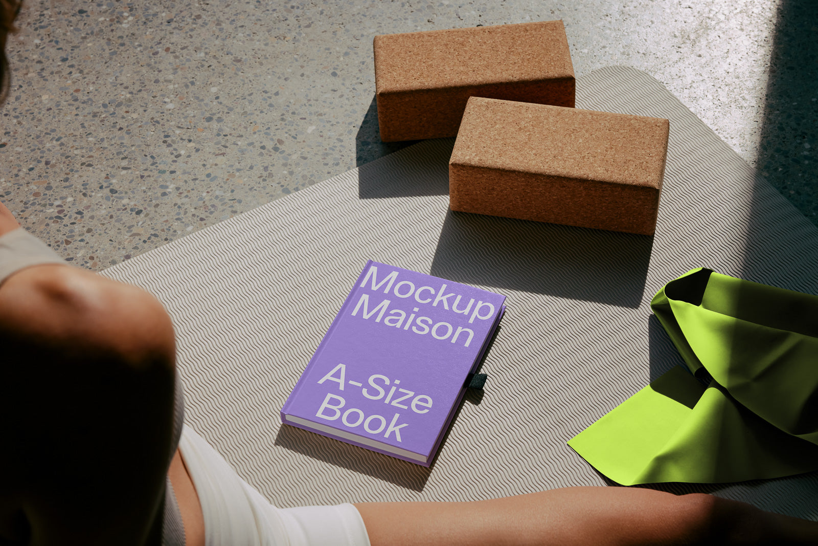 PSD mockup of a purple book with "Mockup Maison A-Size Book" text, resting on a patterned mat with cork blocks and a green fabric nearby.
