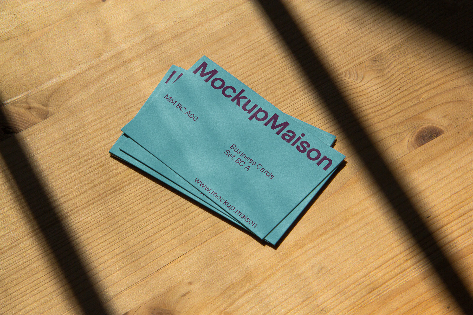 PSD mockup of a stacked set of business cards on a wooden surface, with the text "MockupMaison" and website URL evident in natural light.