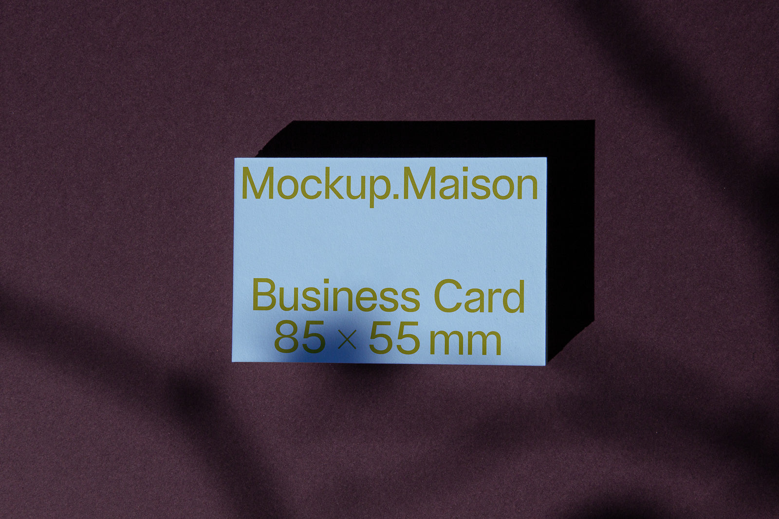 PSD mockup of a business card, dimensions 85 x 55 mm, on a dark textured background with shadows, featuring text "Mockup.Maison" in yellow.