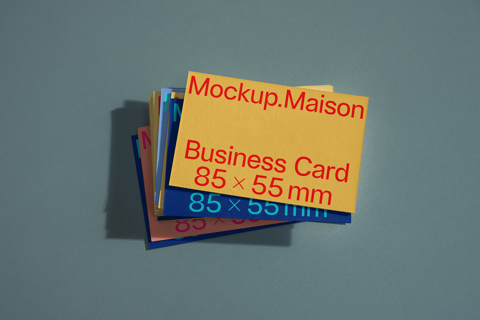 PSD mockup of stacked business cards, top card in yellow with the text "Mockup.Maison Business Card 85 × 55 mm" in red, set against a flat surface.