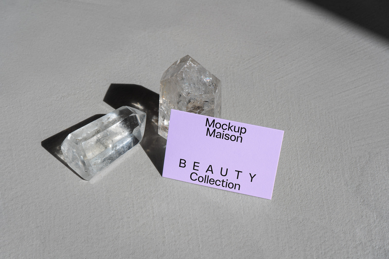 PSD mockup of a business card titled "Beauty Collection" displayed on a textured surface with two clear quartz crystals in natural light.