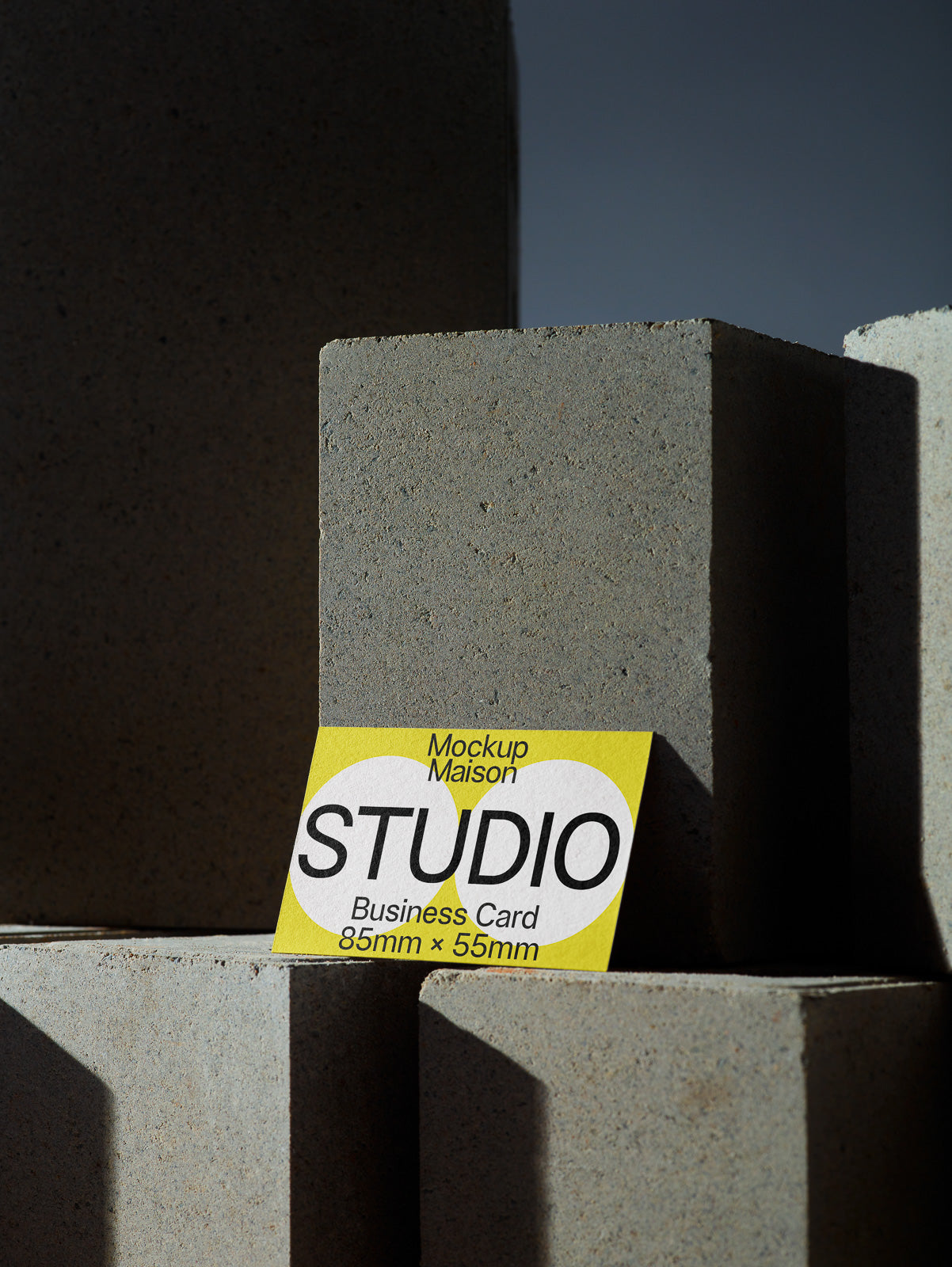 PSD mockup of a business card with "STUDIO" text, featuring dimensions 85mm x 55mm, placed on textured stone blocks under shadowed lighting.