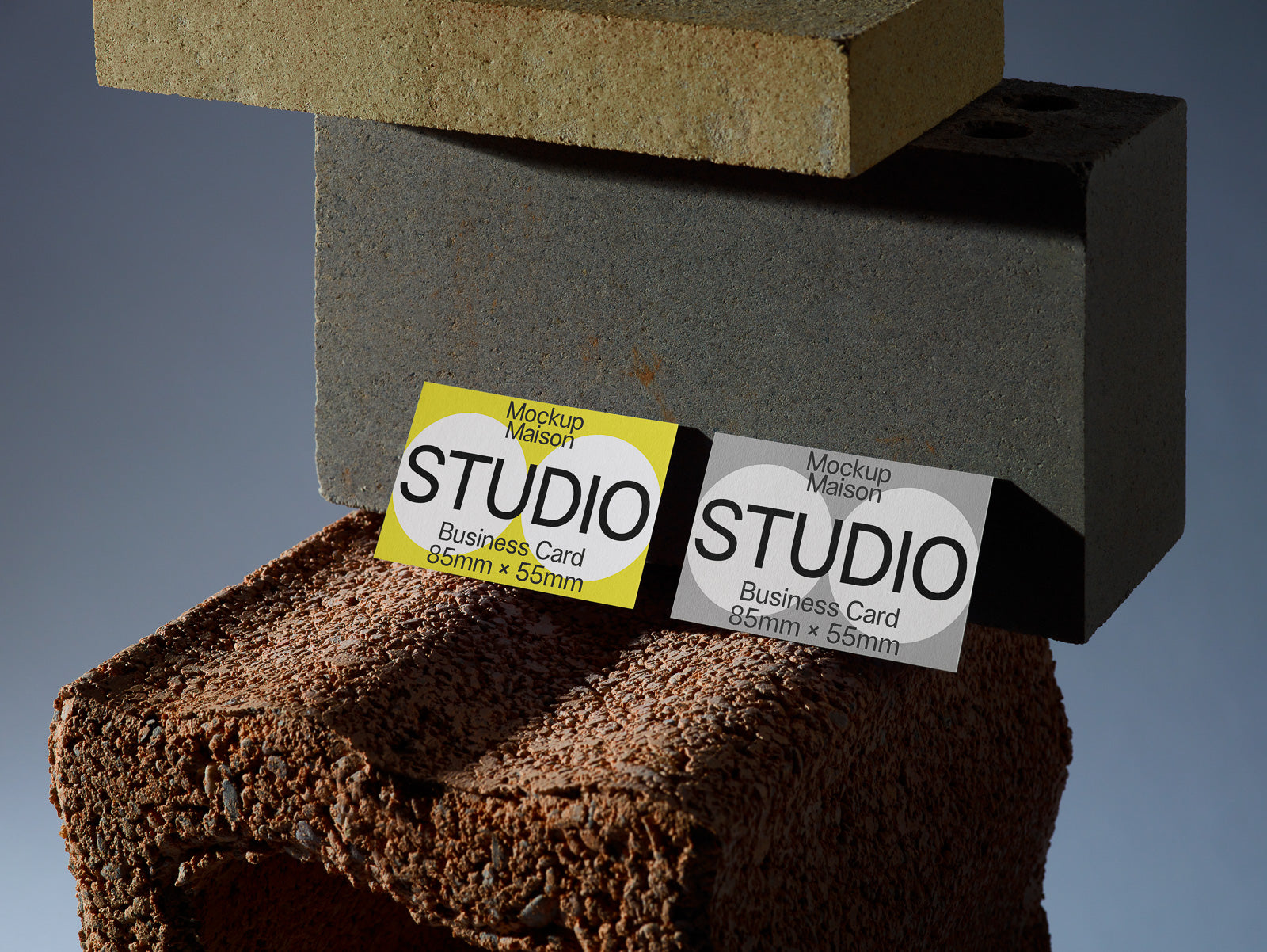 PSD mockup of two business cards displaying "STUDIO" on a textured brick and block background, dimensions 85mm x 55mm, one yellow, one gray.