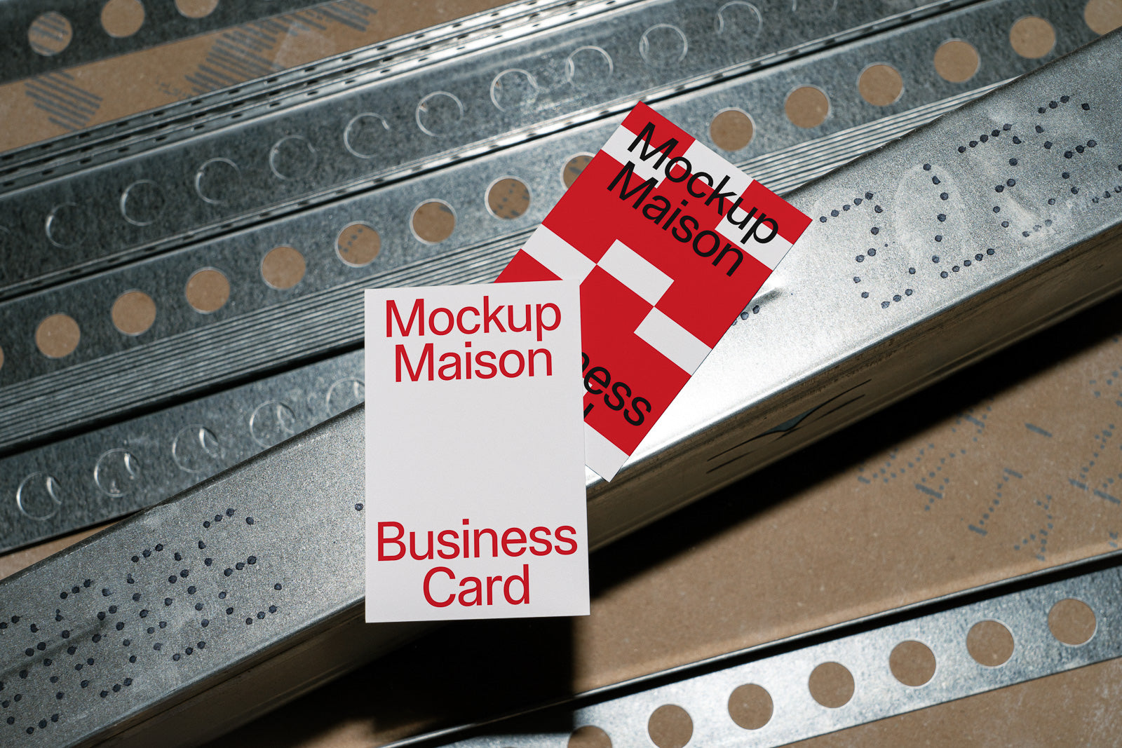 PSD mockup of two business cards with red and white design placed on a metallic surface with a perforated pattern.