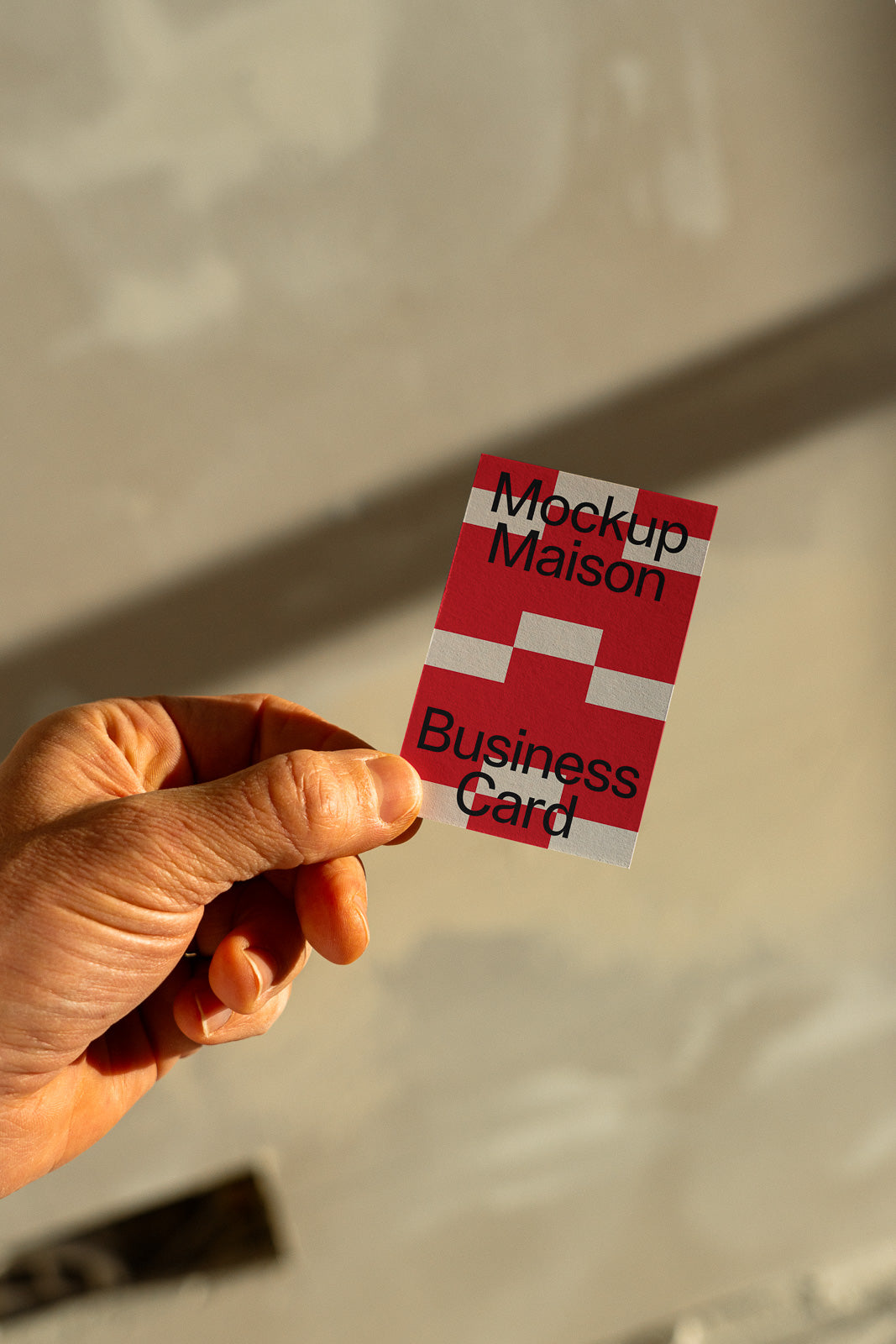 PSD mockup of a business card held in-hand, featuring a red and white geometric design with text, suitable for branding visuals.