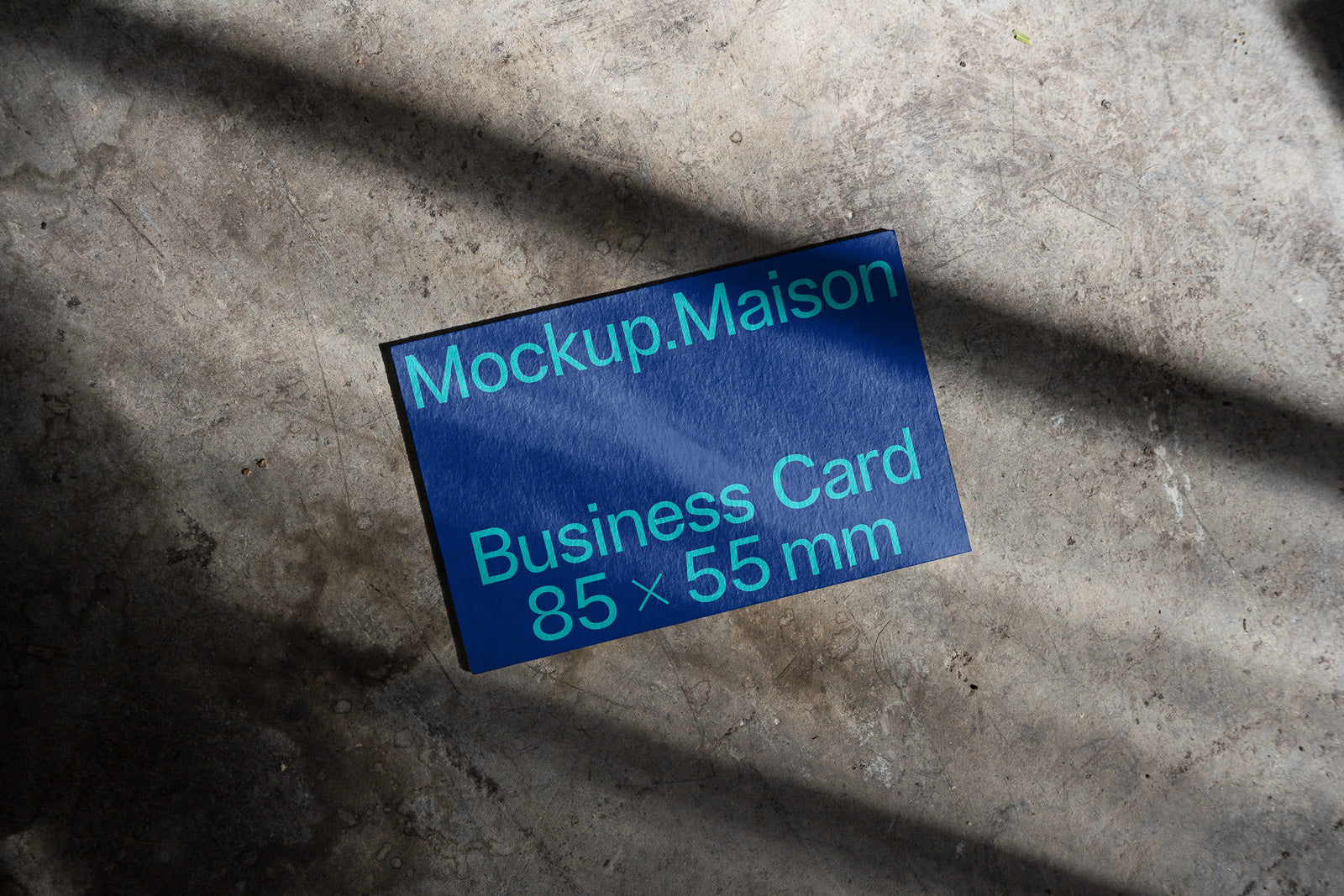 PSD mockup of a blue business card on a textured concrete surface, displaying "Mockup.Maison" and "Business Card 85 x 55 mm" in green text.