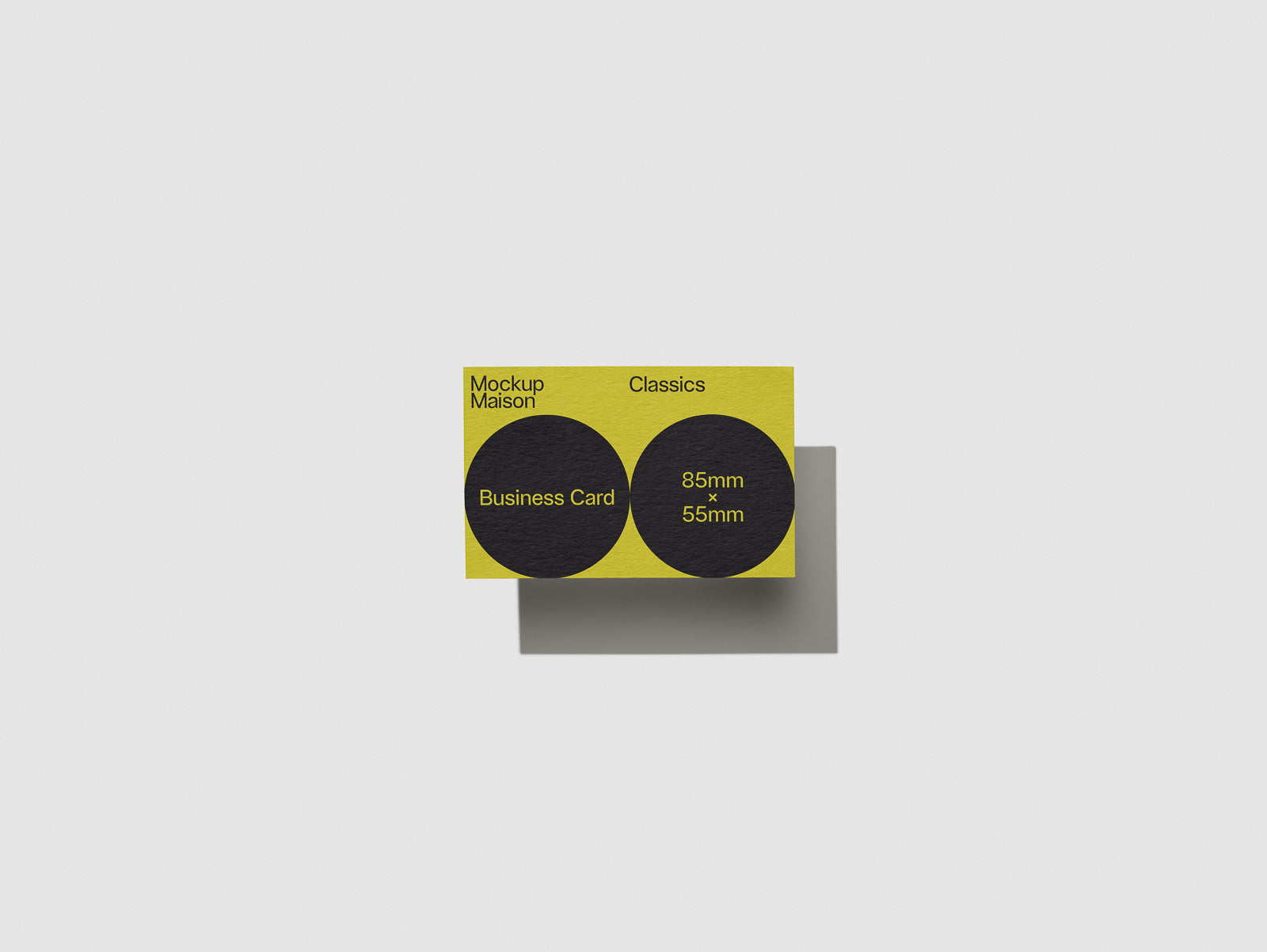 PSD mockup of a yellow business card with black circular design and "Mockup Maison Classics" text. Size dimensions 85mm x 55mm displayed in black text.
