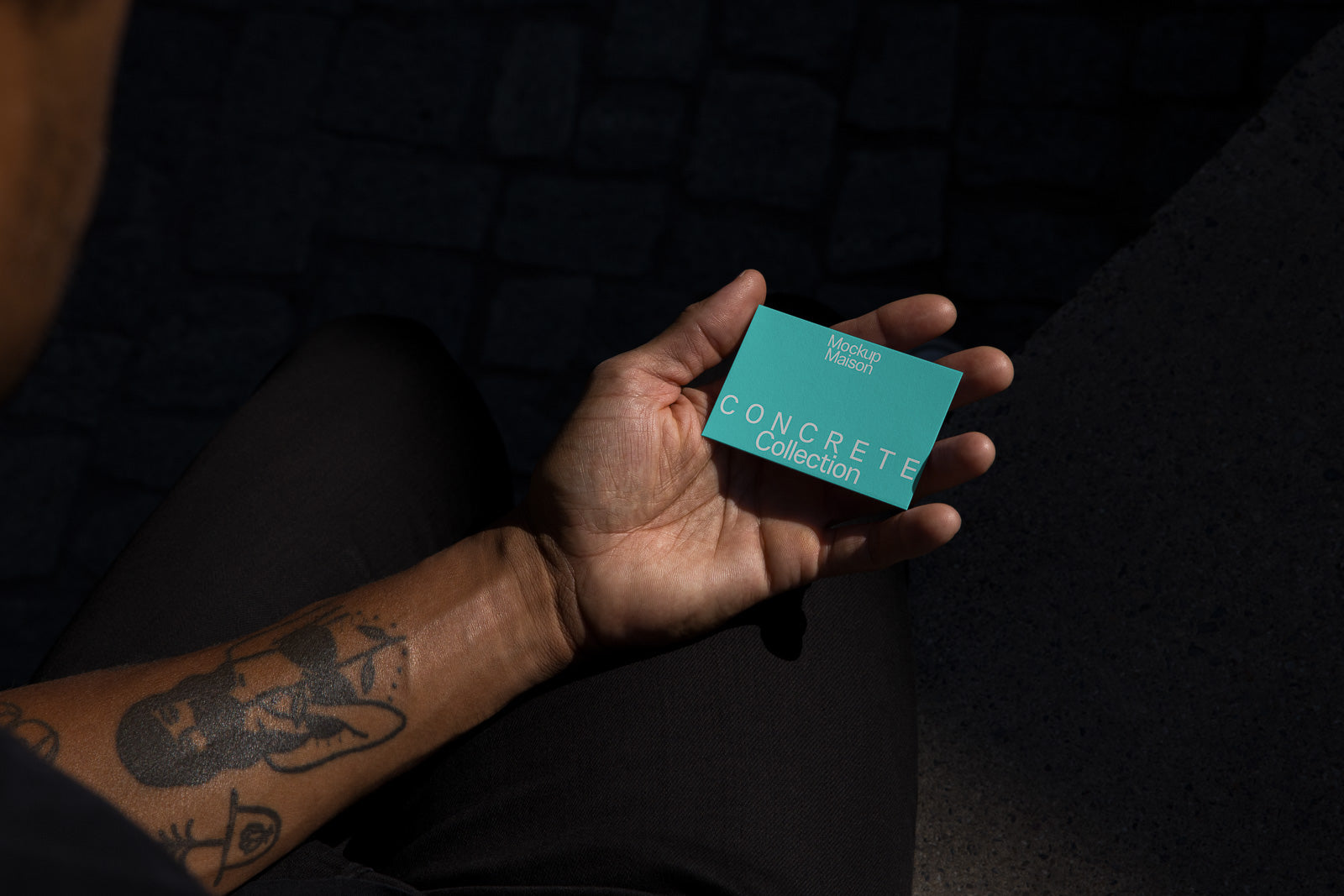 PSD mockup of a hand holding a turquoise business card with text "Concrete Collection" and "Mockup Maison" against a dark background.