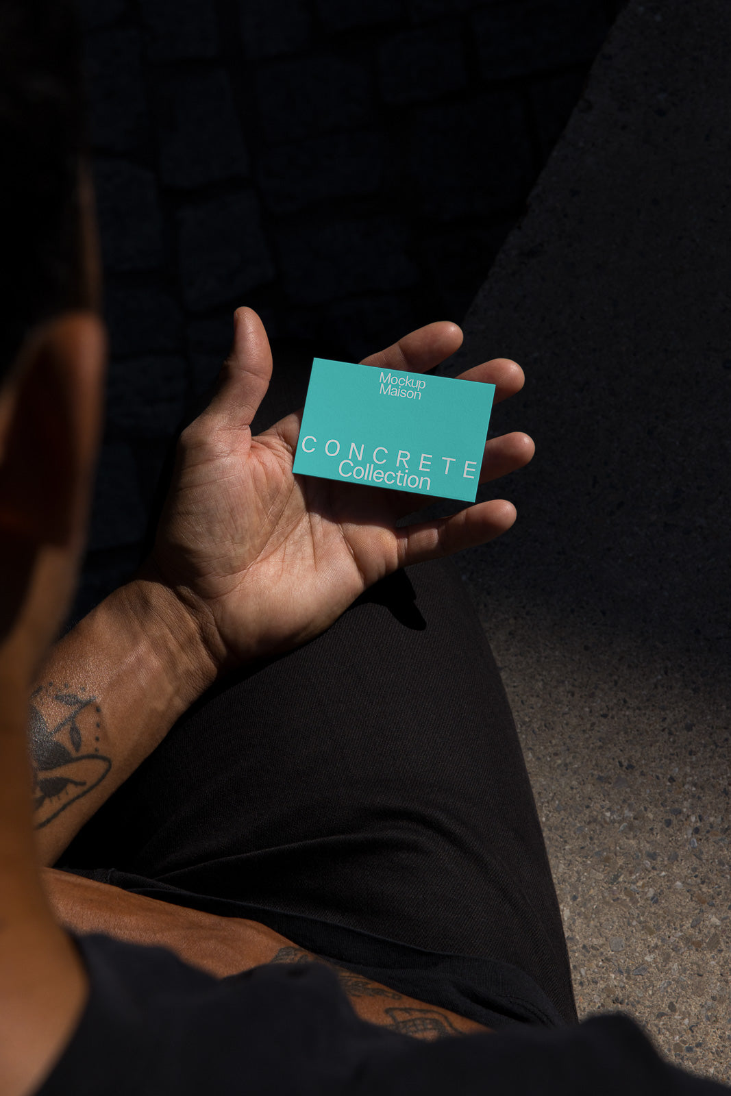 PSD mockup of a person holding a turquoise card titled "Concrete Collection" in a hand, revealing forearm tattoos, set against a dark background.