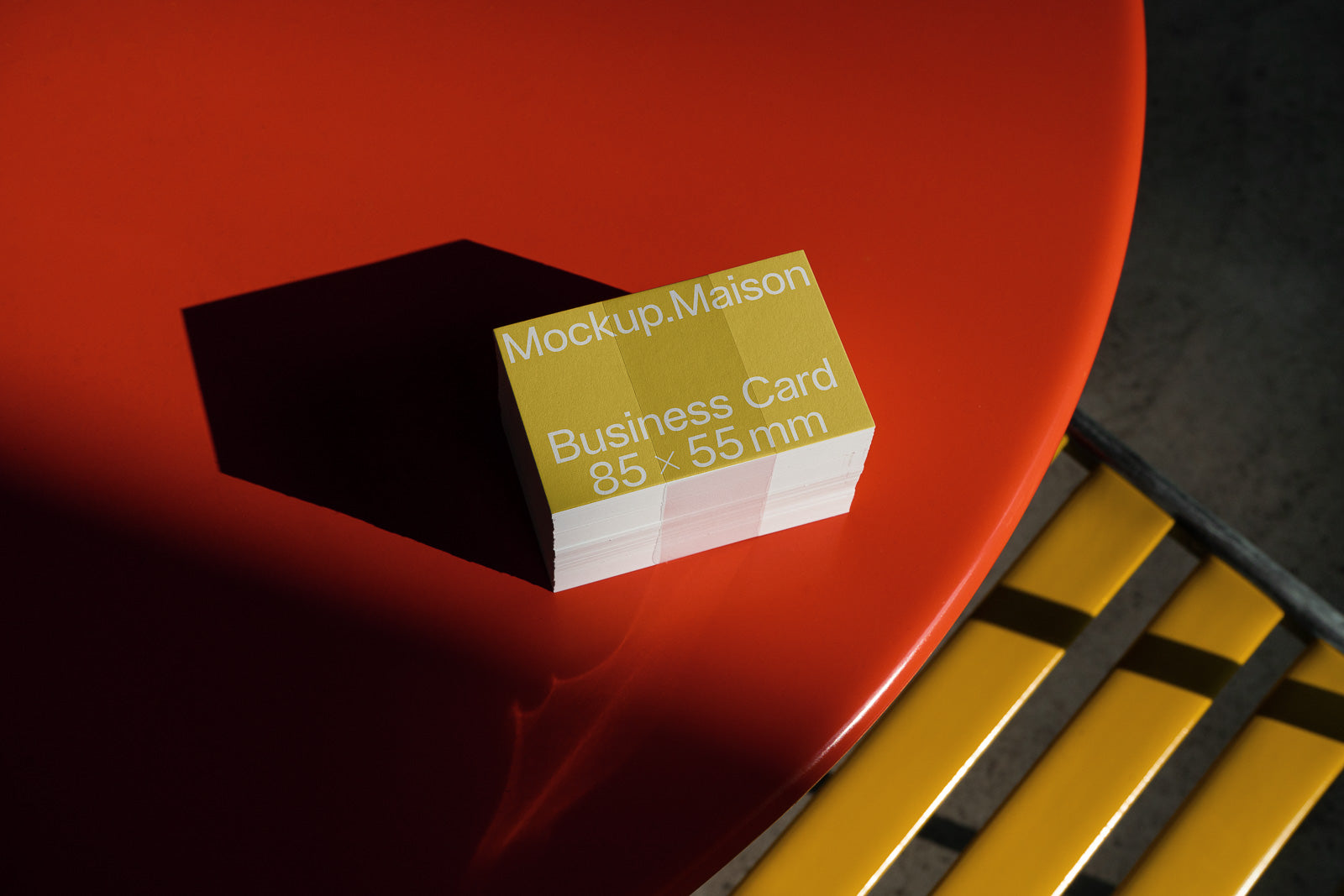 PSD mockup of a stack of business cards, 85 x 55 mm, on a brightly lit red surface with yellow and gray accents in the background.