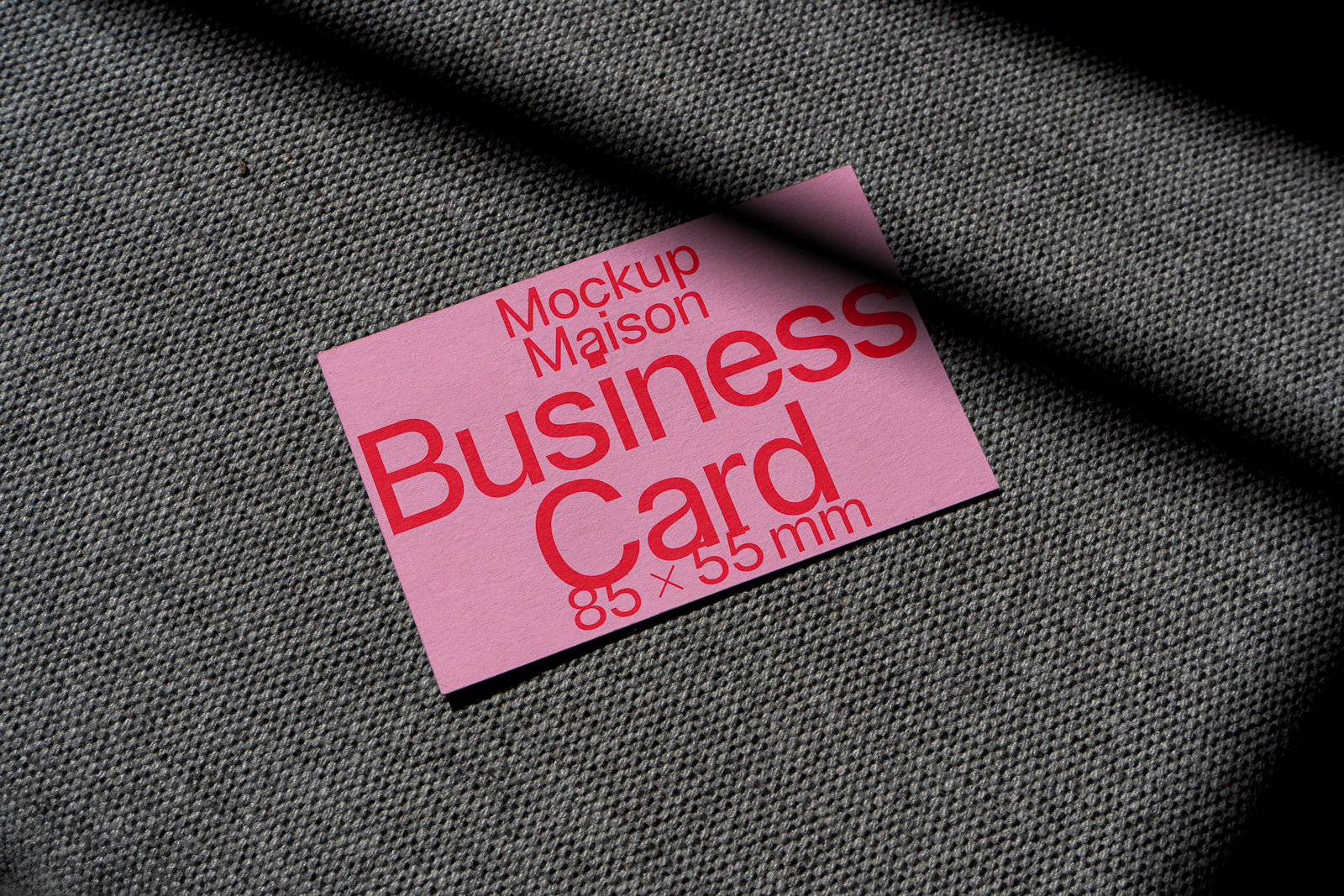 PSD mockup of a pink business card labeled "Mockup Maison Business Card 85 x 55 mm" on textured dark fabric with light shadow.