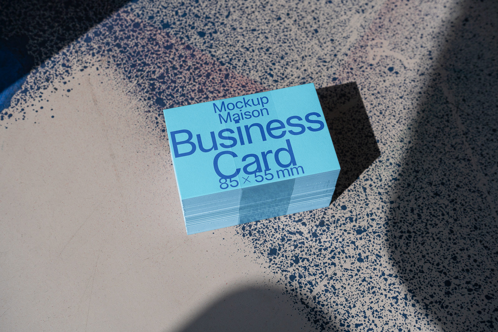 PSD mockup of a stack of blue business cards with "Mockup Maison Business Card 85 x 55 mm" text, placed on a textured surface with shadow contrast.