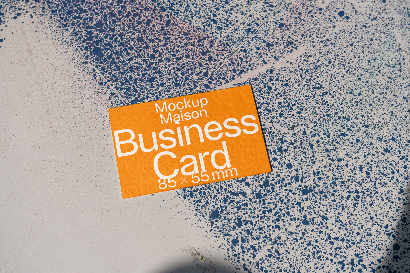 PSD mockup of an orange business card measuring 85 x 55 mm placed on a speckled blue and white textured background.