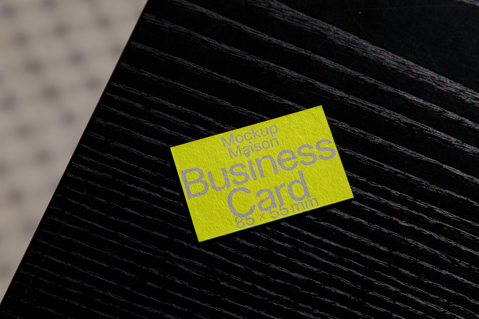 PSD mockup of a neon yellow business card on a textured black surface, displaying "Mockup Maison Business Card 85 x 55 mm" in gray text.