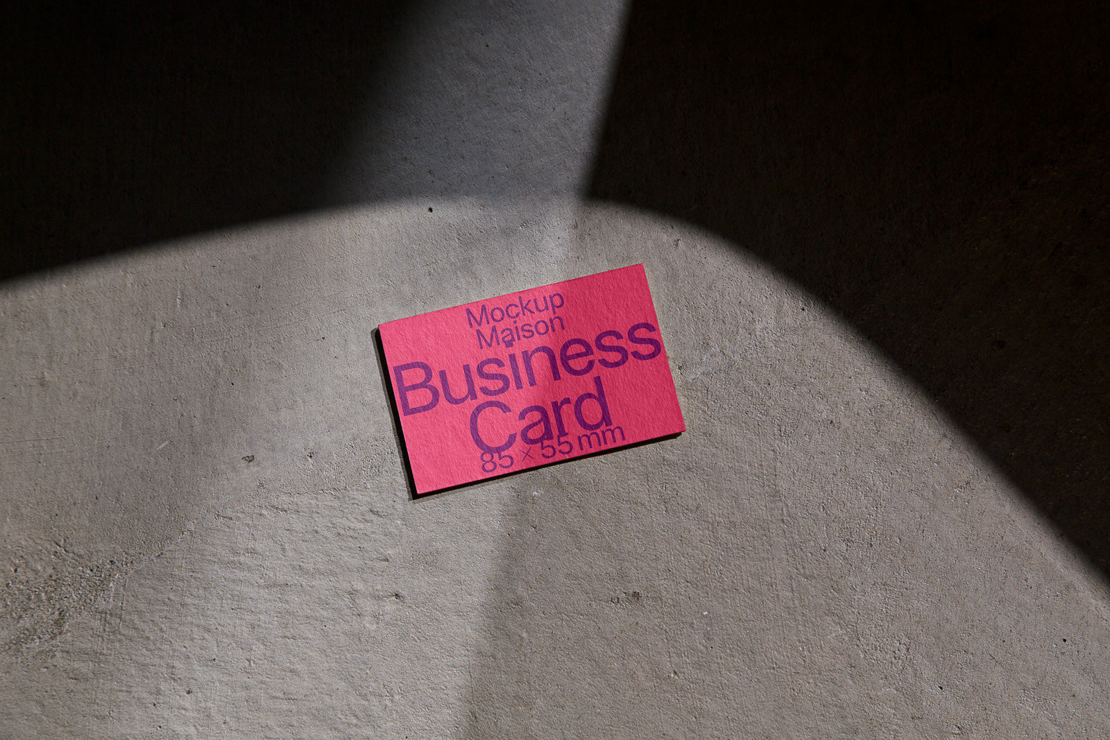 PSD mockup of a red business card on a textured concrete surface, angled light creating shadows, with text reading "Mockup Maison Business Card 85 x 55 mm."