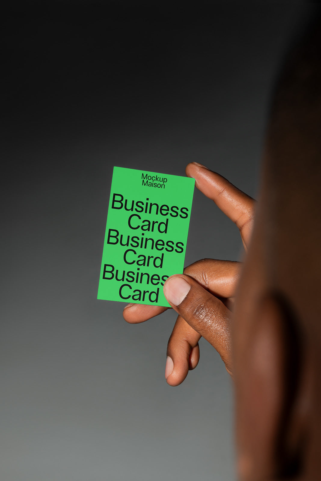 PSD mockup of a hand holding a green business card with the text "Mockup Maison Business Card" on a neutral background.