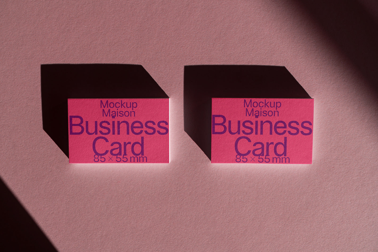 PSD mockup of two pink business cards with purple text, arranged on a pink surface casting long shadows. The text includes dimensions 85×55 mm.