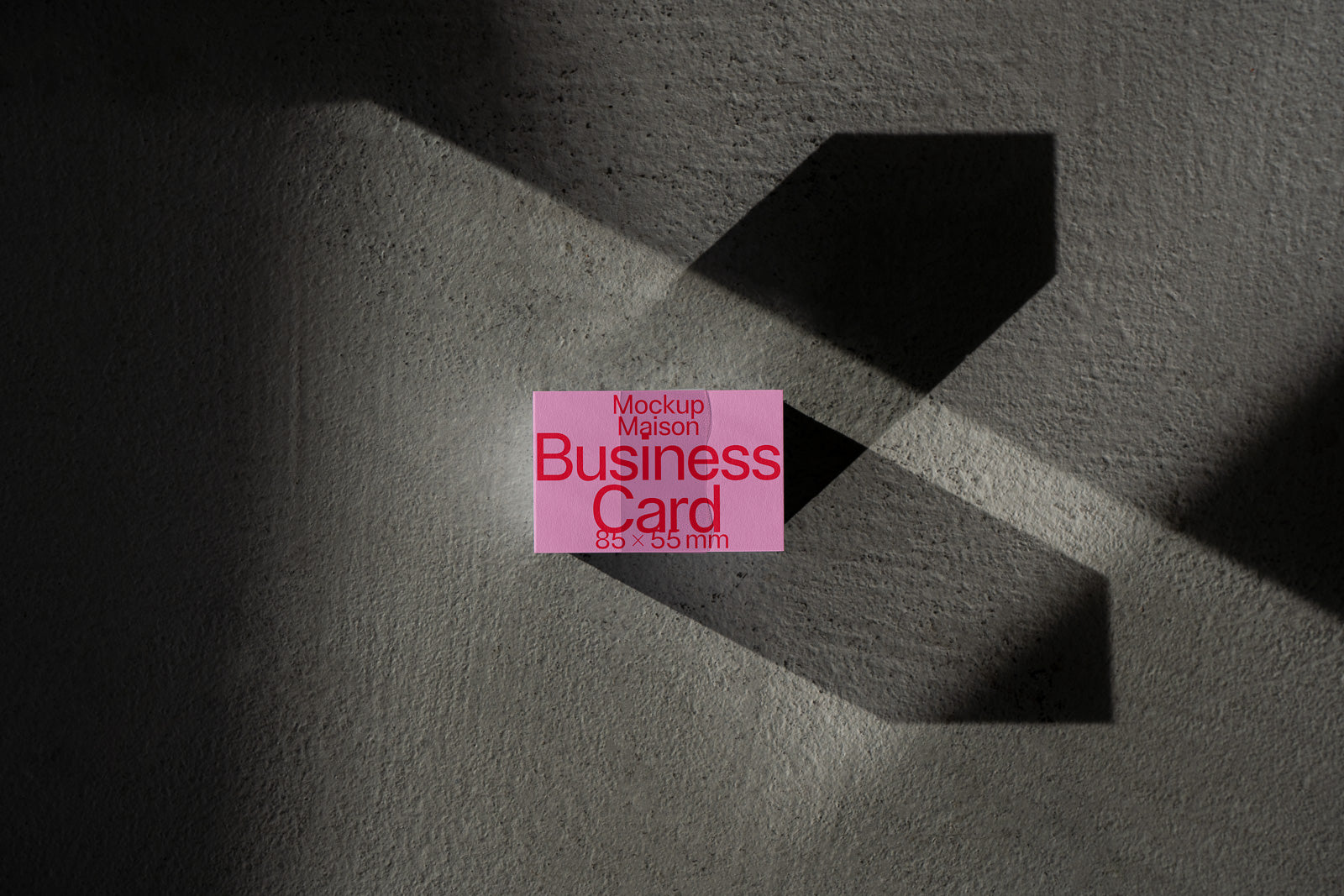 PSD mockup of a pink business card on a textured surface with shadows, displaying text "Mockup Maison Business Card 85 x 55 mm" in red font.