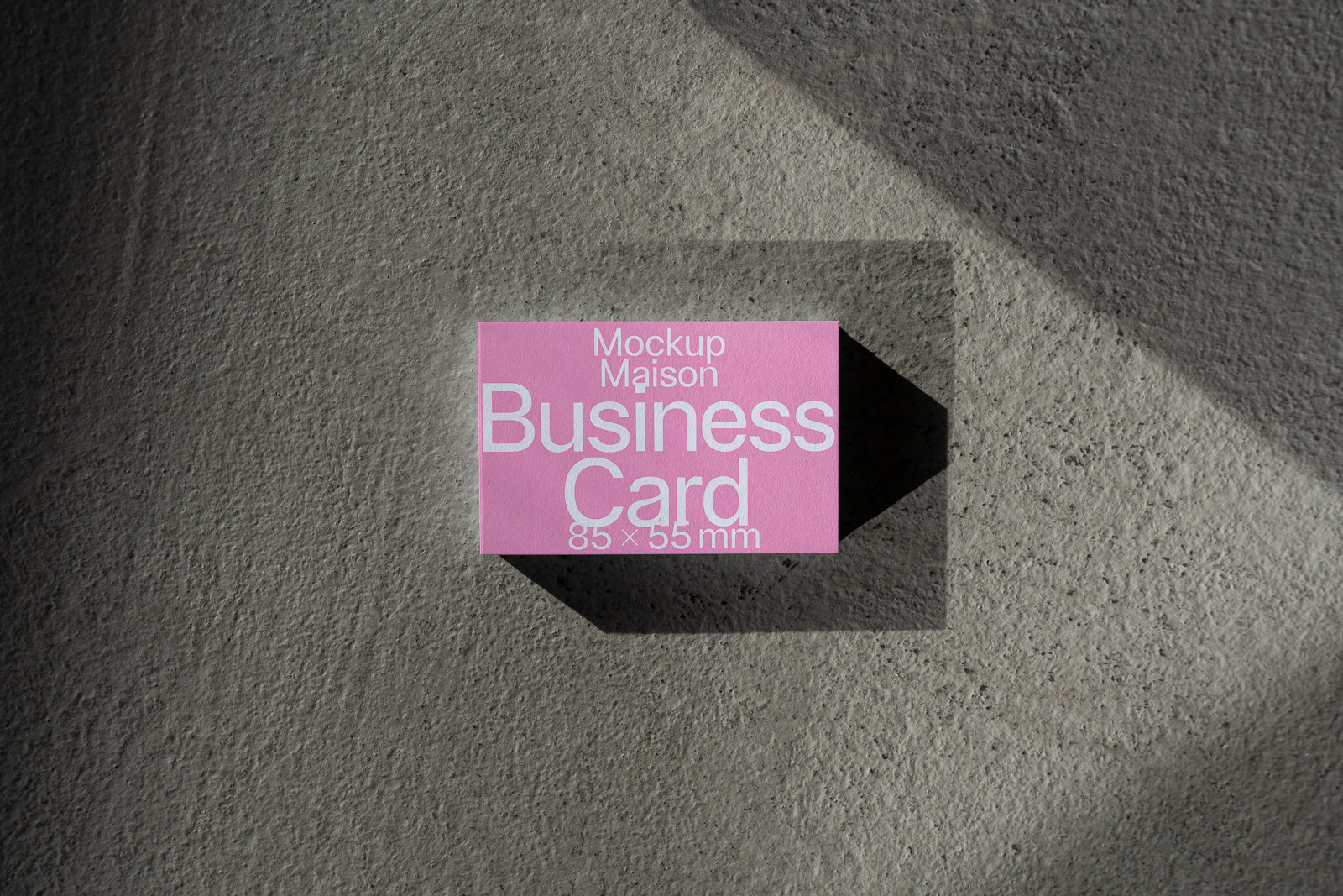 PSD mockup of a pink business card with large white text displaying dimensions 85x55 mm, placed on a textured surface with light and shadow play.