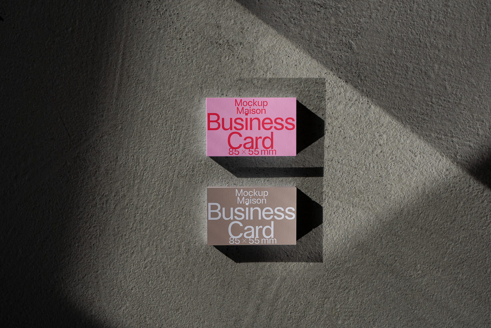 PSD mockup of two business cards on a textured surface, one pink with red text, the other beige with white text, both displaying dimensions 85×55 mm.