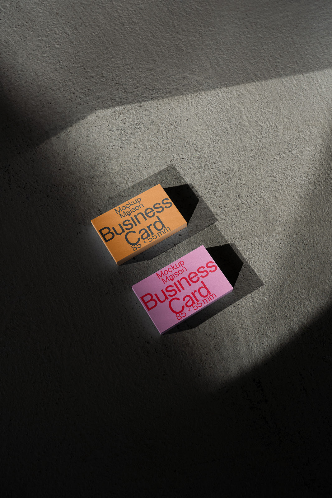 PSD mockup of two business card boxes on a textured surface, one in orange and the other in pink, with shadows creating a play of light, dimensions 85 × 55 mm.
