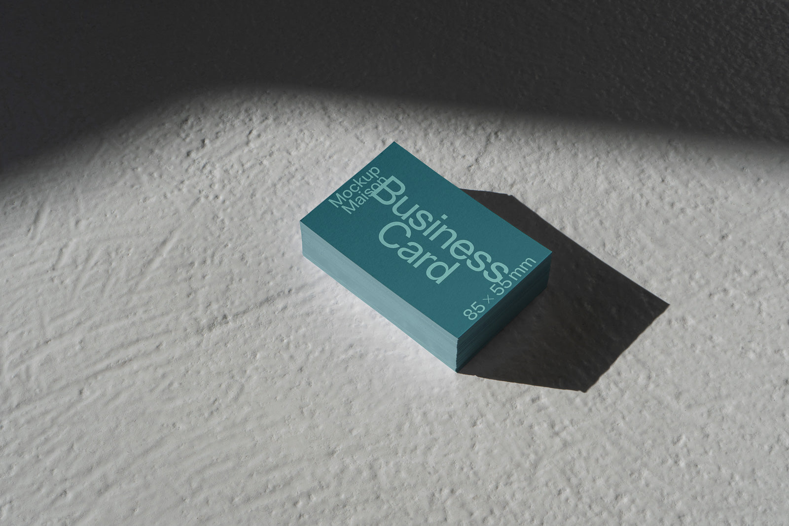 PSD mockup of a stack of business cards labeled "85 x 55 mm" with a teal design on a textured surface, casting a shadow.