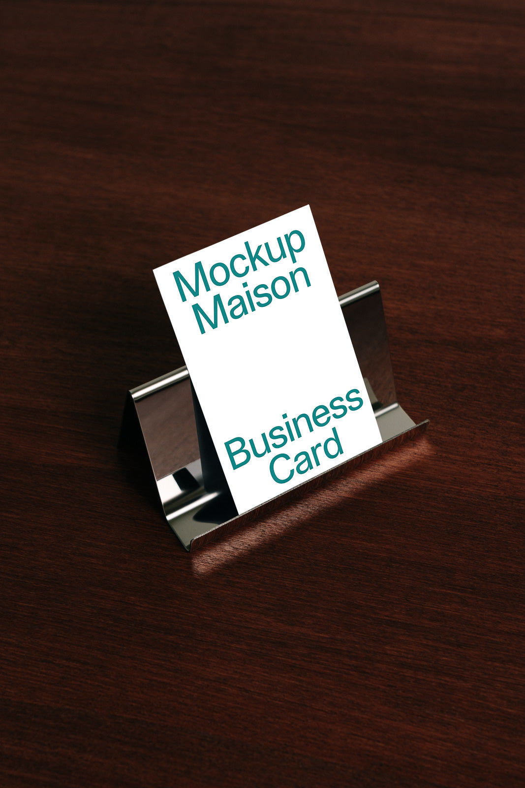 PSD mockup of a business card displayed in a metal holder on a wooden surface, featuring the text "Mockup Maison Business Card" in green font.