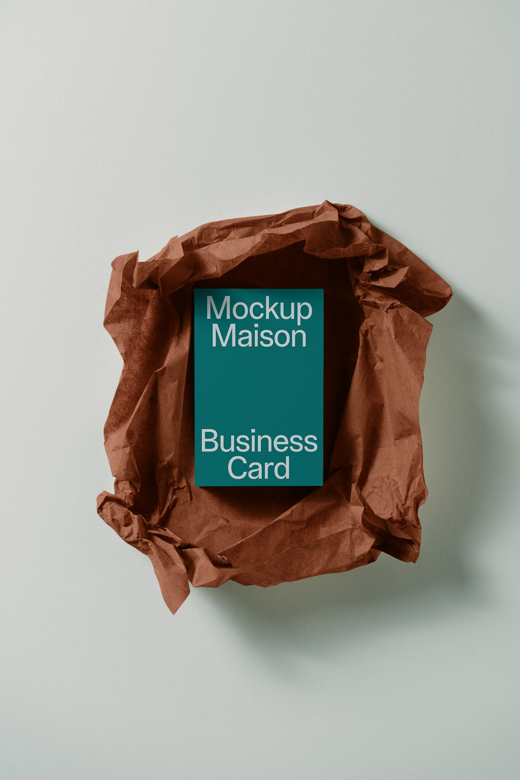 PSD mockup of a teal business card labeled "Mockup Maison" placed on crumpled brown paper, providing a minimalist presentation backdrop.