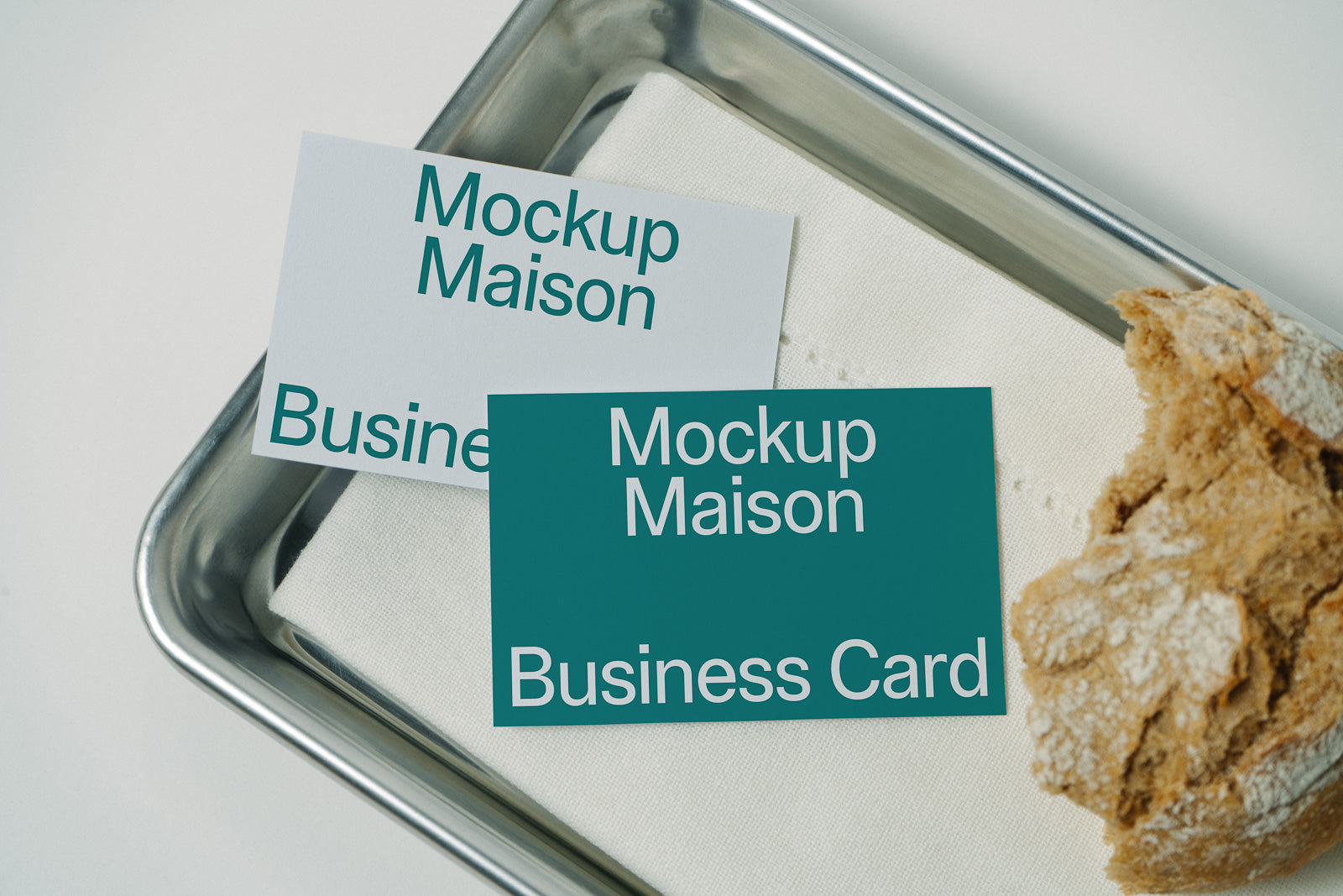 PSD mockup of two business cards printed with "Mockup Maison" placed on a metal tray with a linen napkin and a piece of bread.
