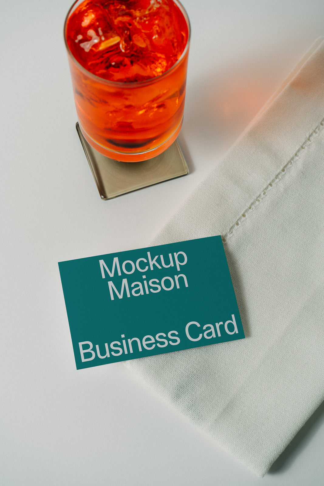 PSD mockup of a business card placed next to an orange drink on a metal coaster and a folded white napkin.
