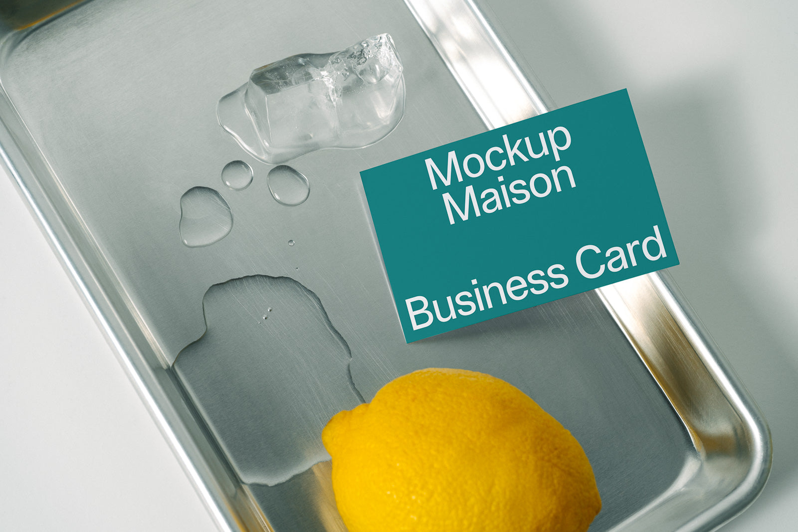 PSD mockup of a business card placed on a metallic tray with ice cubes and a lemon, showcasing a sleek, minimalistic design style.